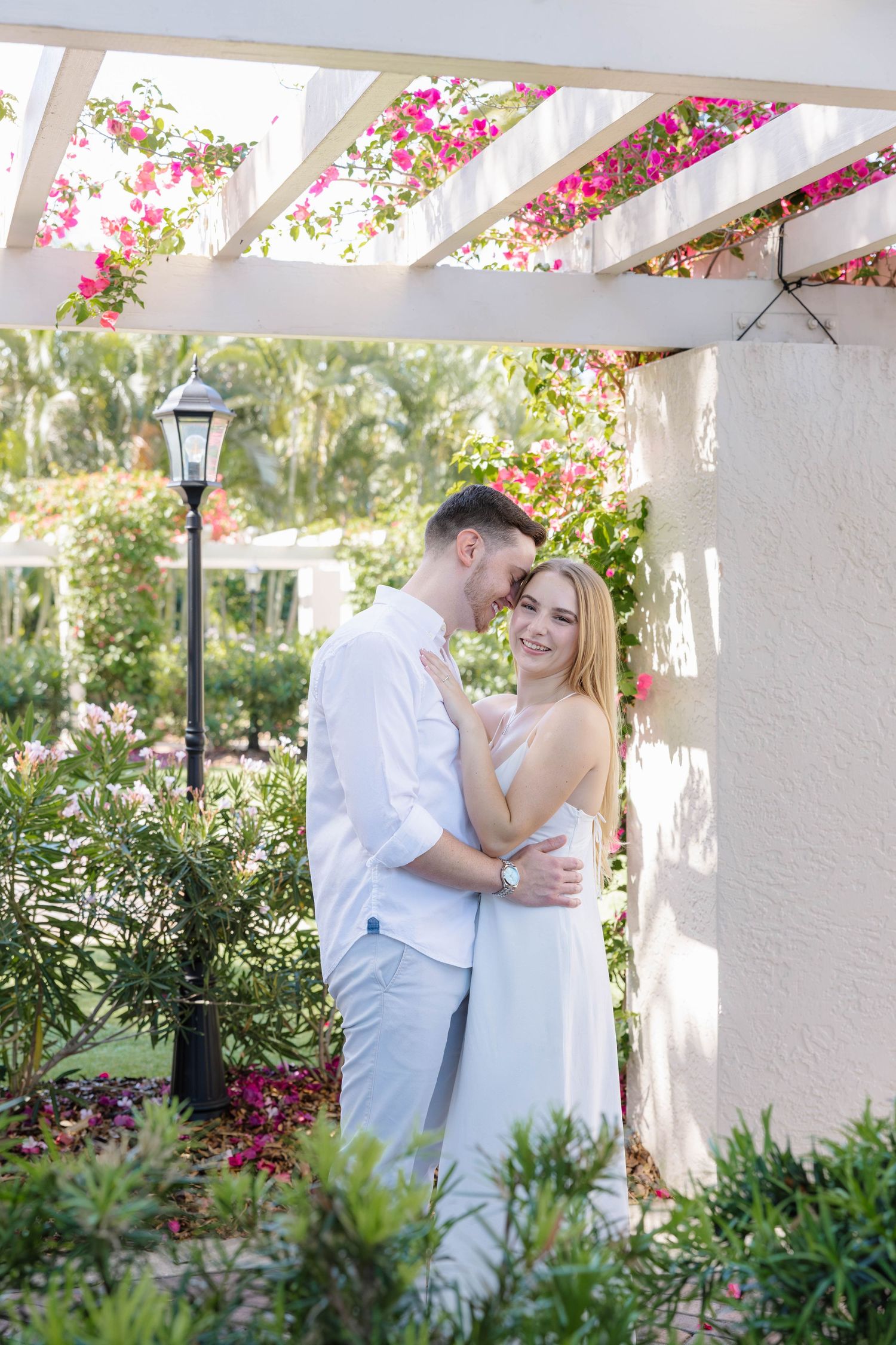 Couple embracing under a white pergola surrounded by colorful bougainvillea.