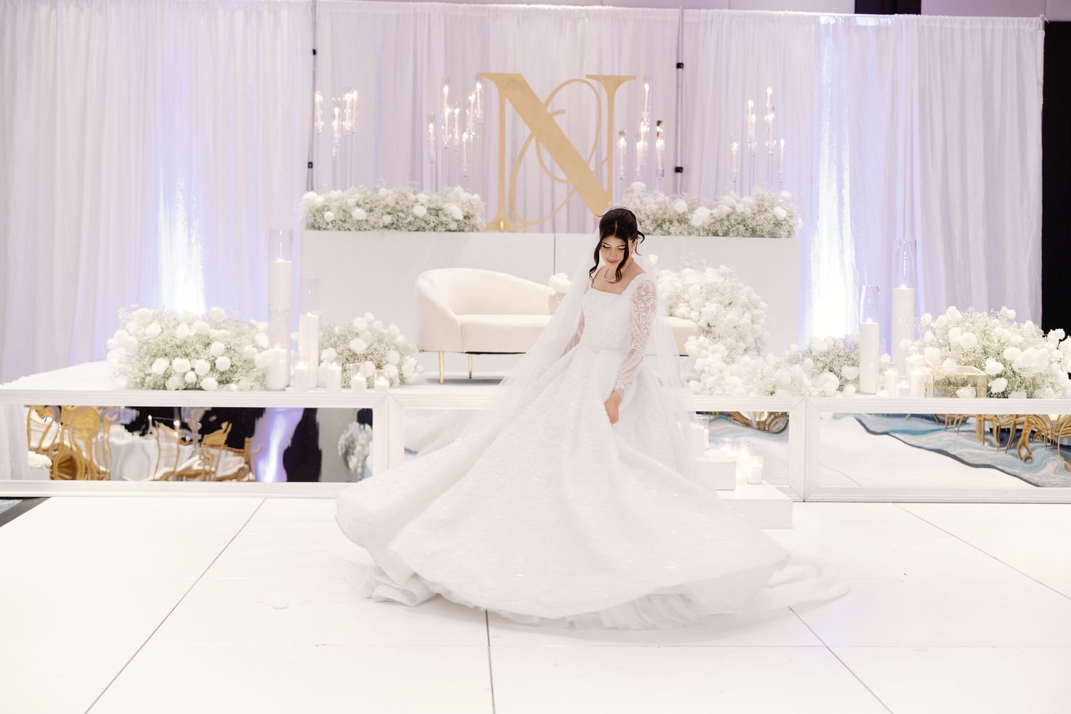 Bride in a flowing white ballgown twirls on a white dance floor at an elegant all-white wedding reception.