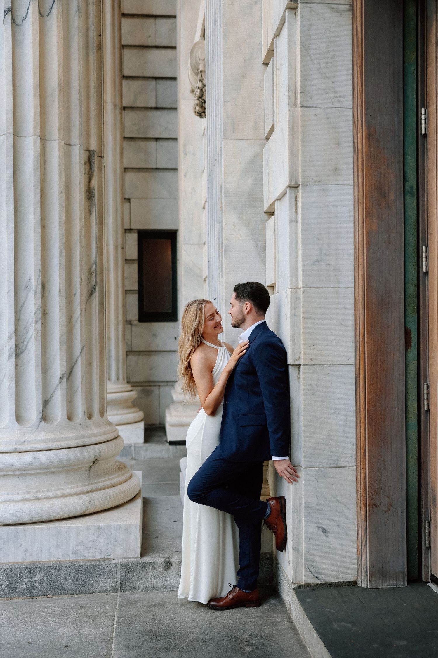 Bride and groom sharing an intimate moment between marble columns of a grand historic building.
