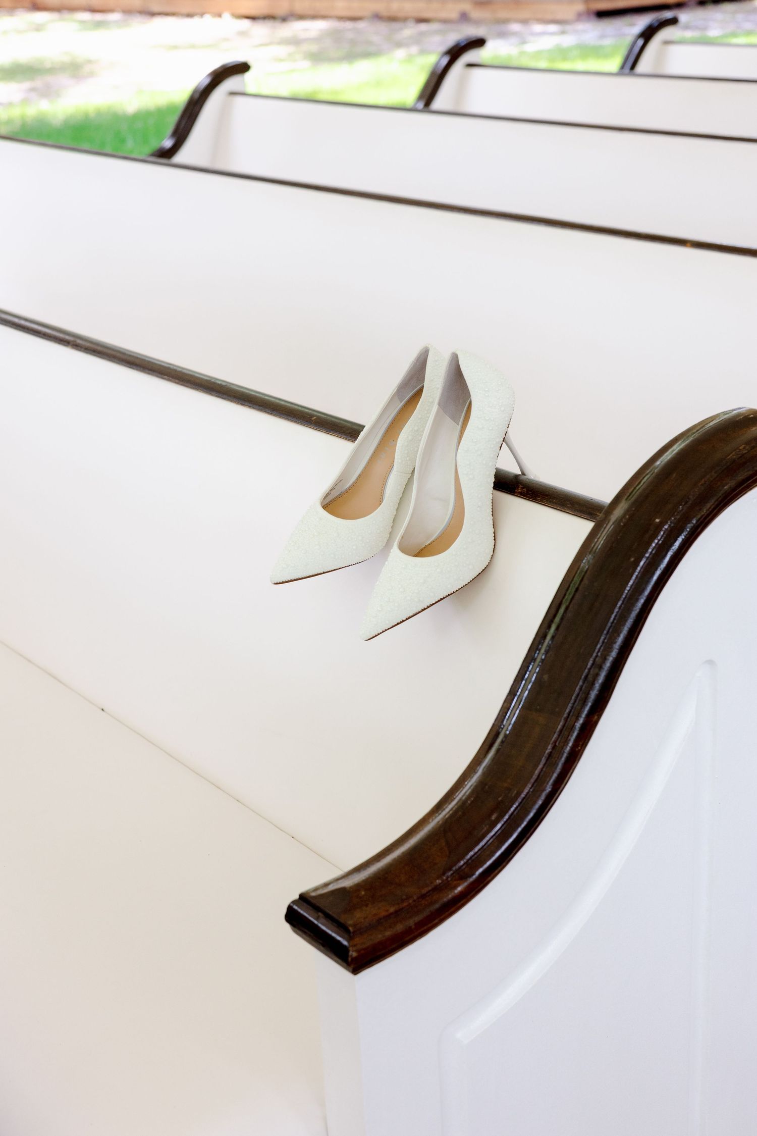 White bridal heels resting on a wooden church pew arm before the wedding ceremony.