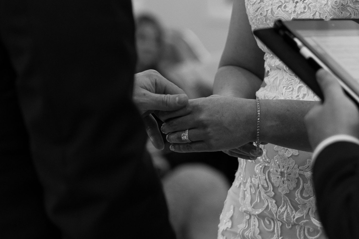 A black and white close-up of a groom placing a wedding ring on the bride's hand.