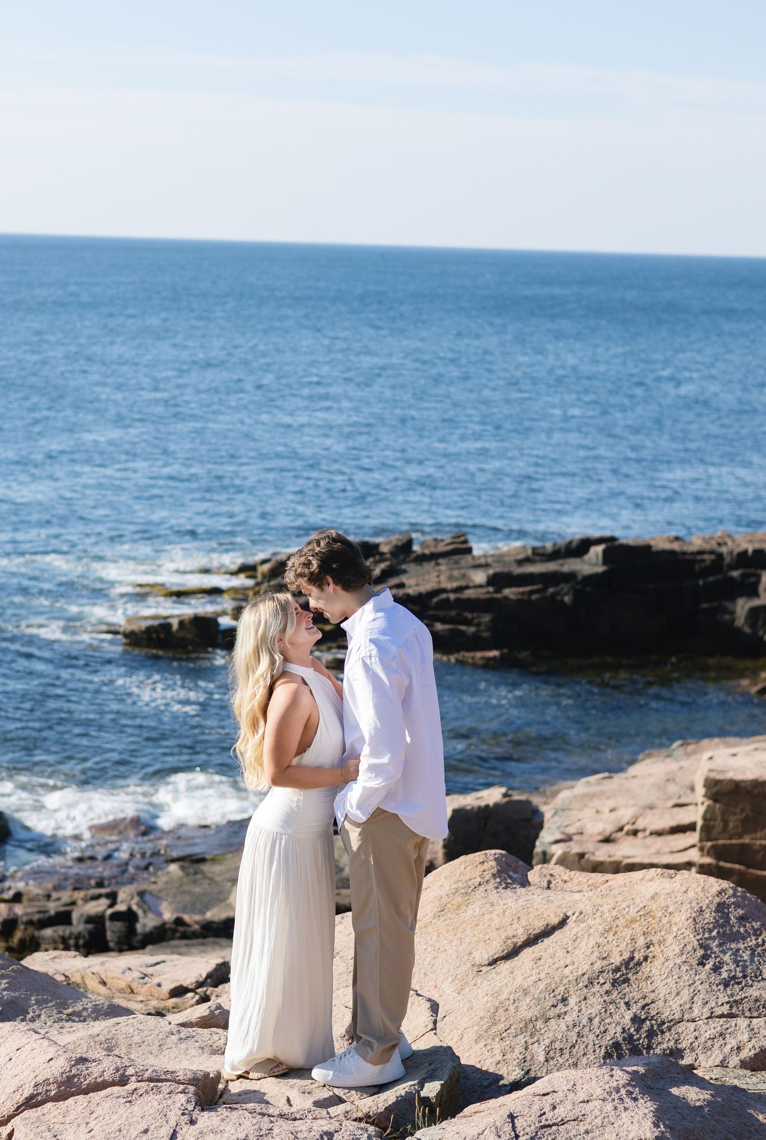 Couple sharing a kiss on rocky coastal cliffs with deep blue ocean waves in the background.