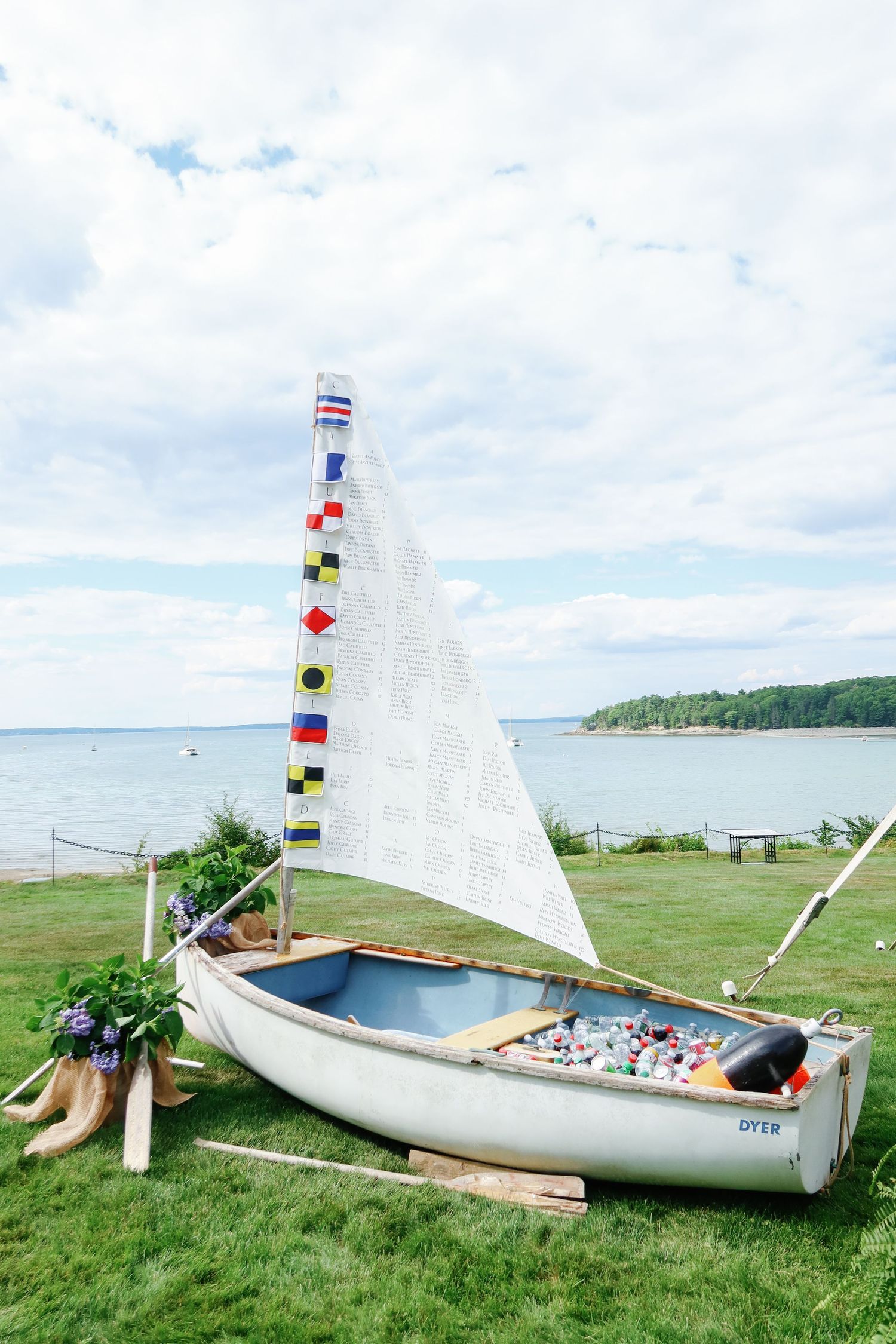 Vintage sailboat used as creative wedding seating chart display with nautical flags and floral decor by waterfront.