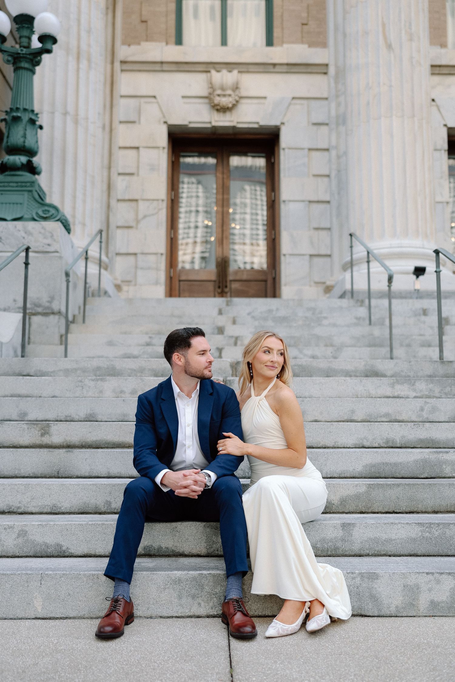 Bride and groom sitting on steps of a grand neoclassical building gazing at each other lovingly.