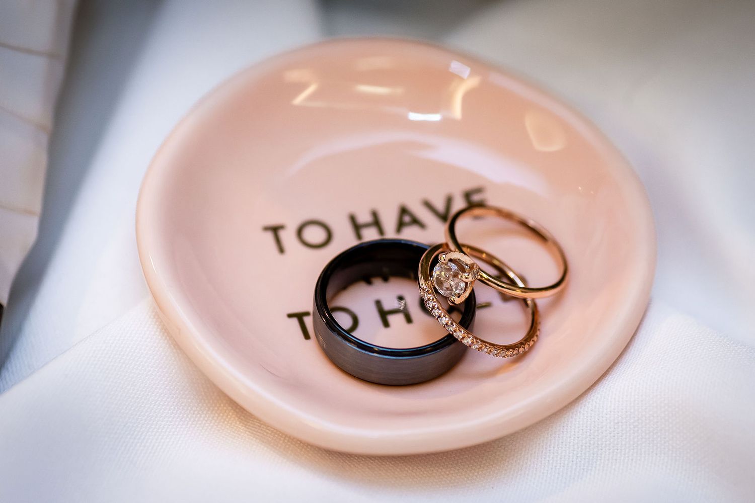 Wedding rings displayed on a pink ceramic dish inscribed with To Have and To Hold.