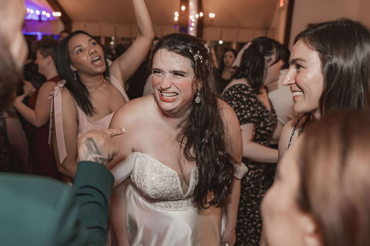 Bride dancing joyfully with guests at lively indoor wedding reception celebration.