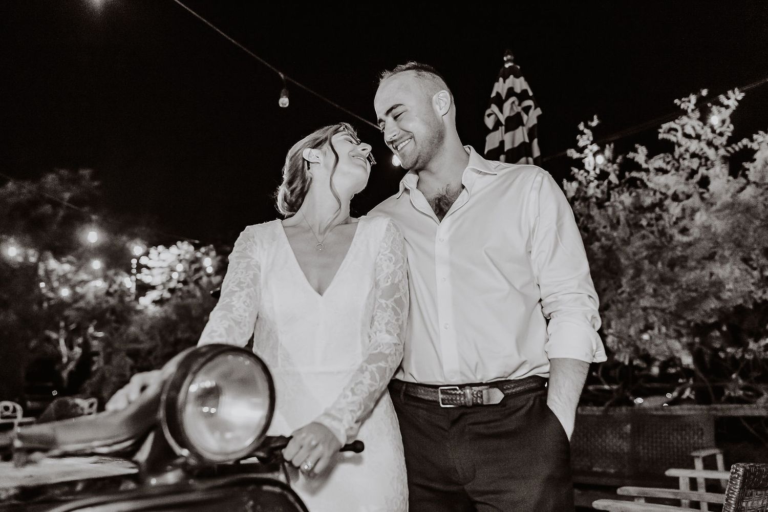 Black and white photo of a tattooed bride and groom sharing a romantic moment at night near a vintage car.