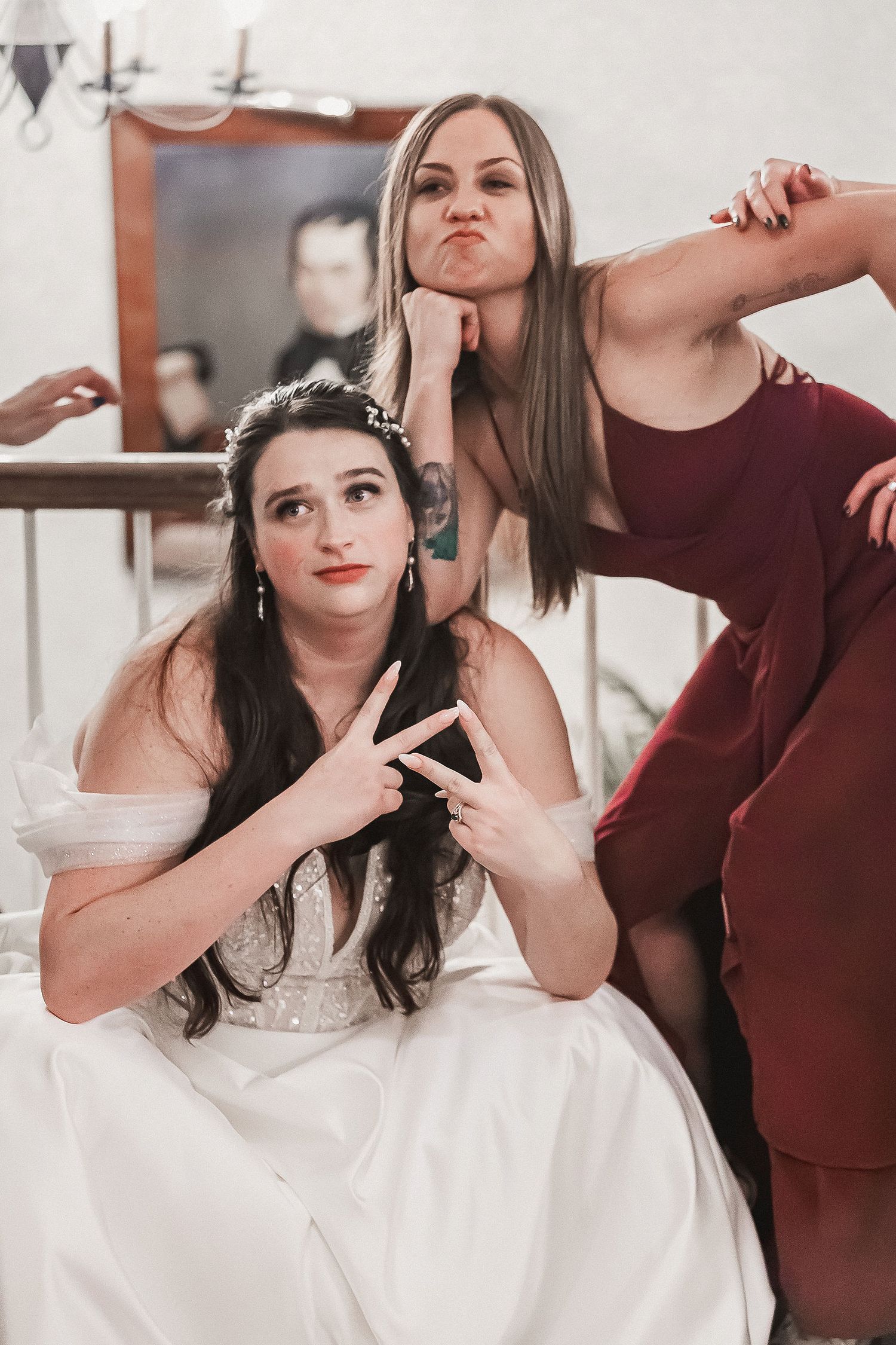 Bride and bridesmaid in burgundy dress making fun poses together before the wedding.