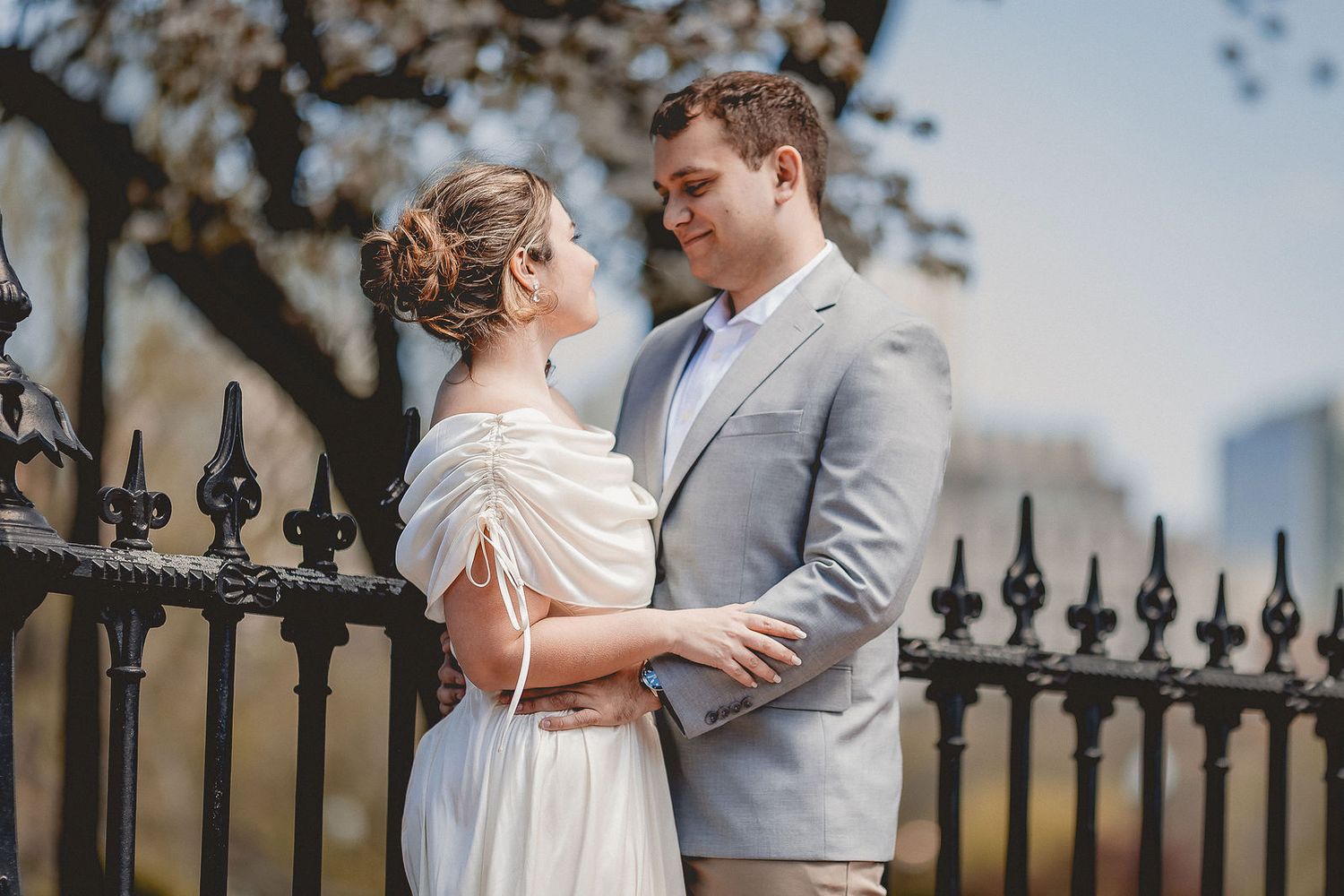 Elegant couple embracing near ornate iron fence during outdoor spring engagement portrait session.