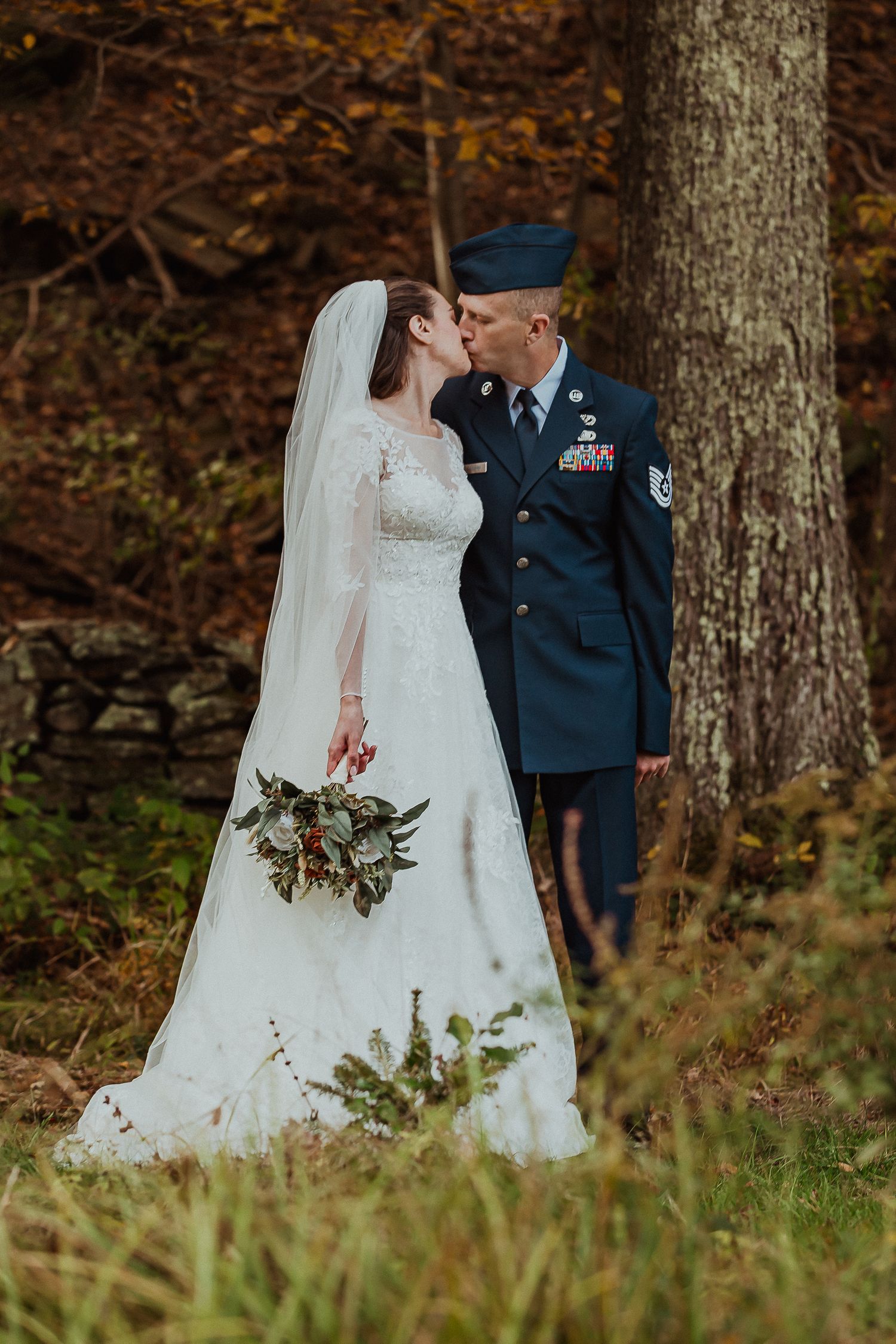 Bride and groom kissing by a tree, groom in military uniform.