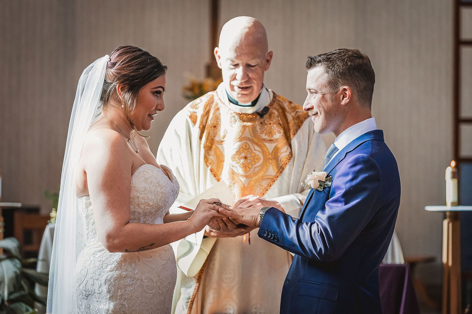 Bride and groom exchange rings during a church wedding ceremony with a priest in gold vestments.