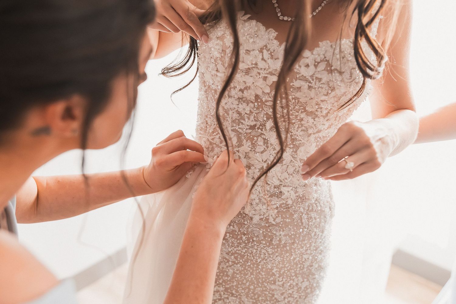 Bridesmaid fastening buttons on bride's lace wedding gown.