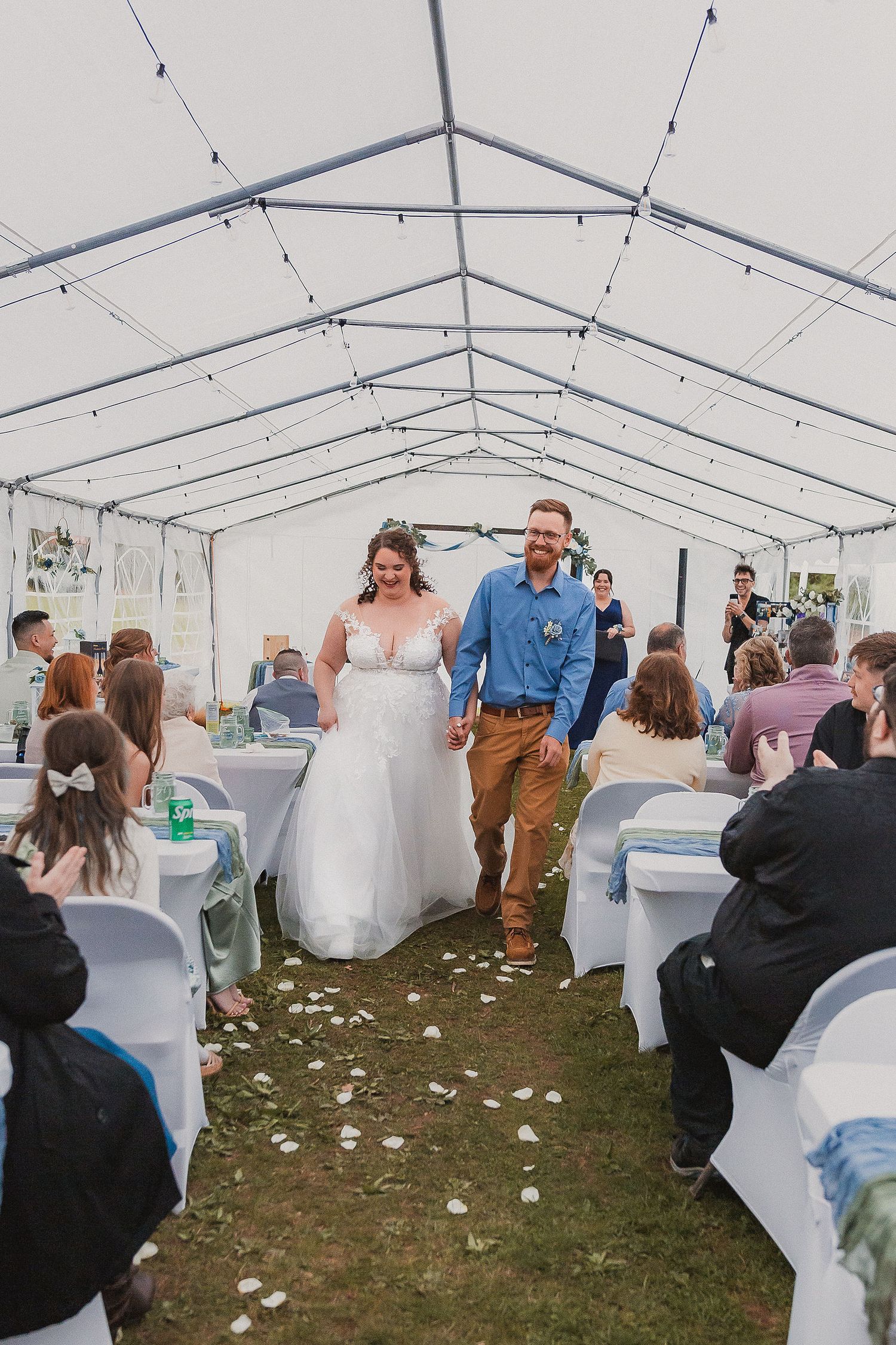Newlyweds walking joyfully down the aisle under a white tent wedding ceremony.