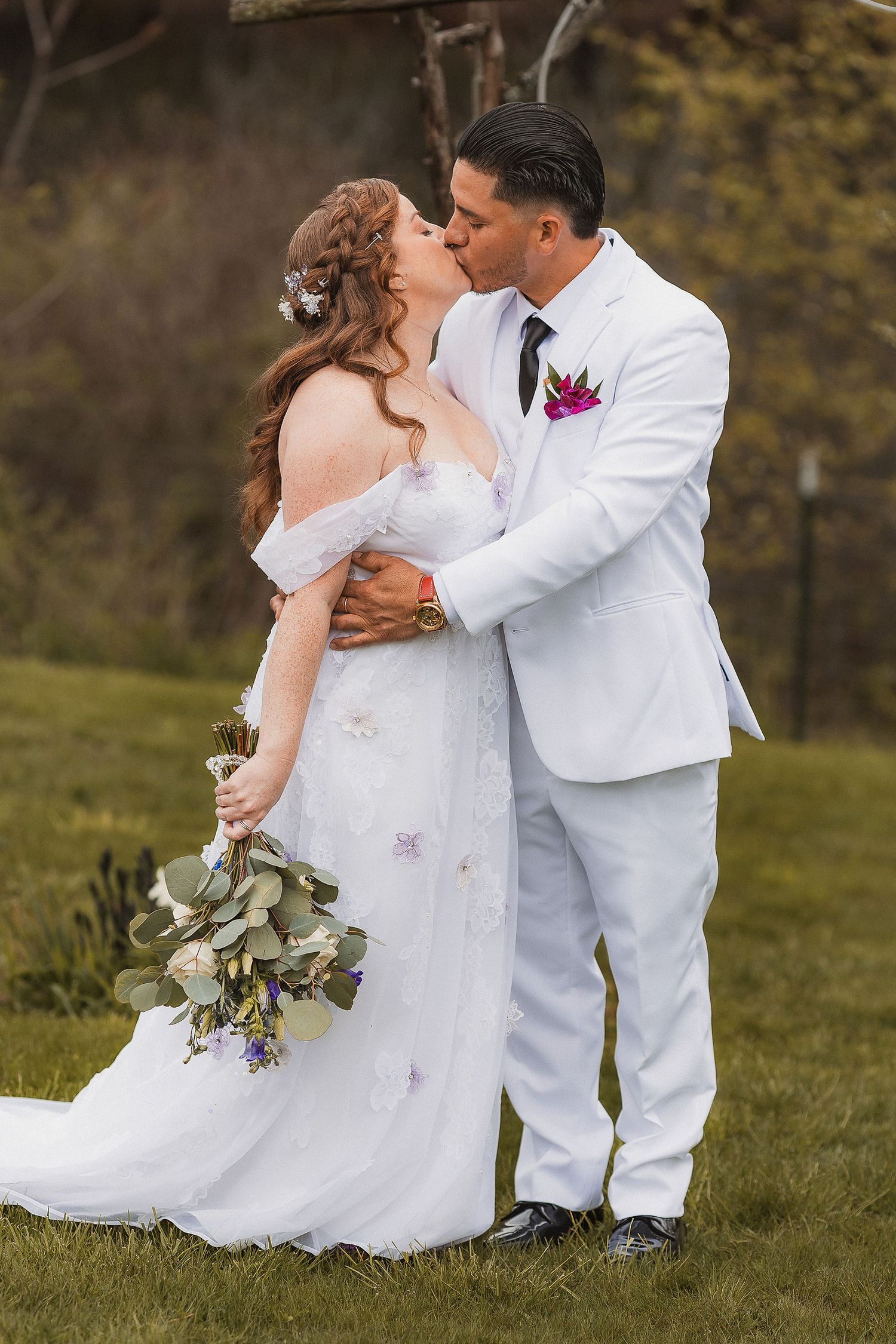 Bride and groom sharing romantic kiss outdoors with lush greenery background.
