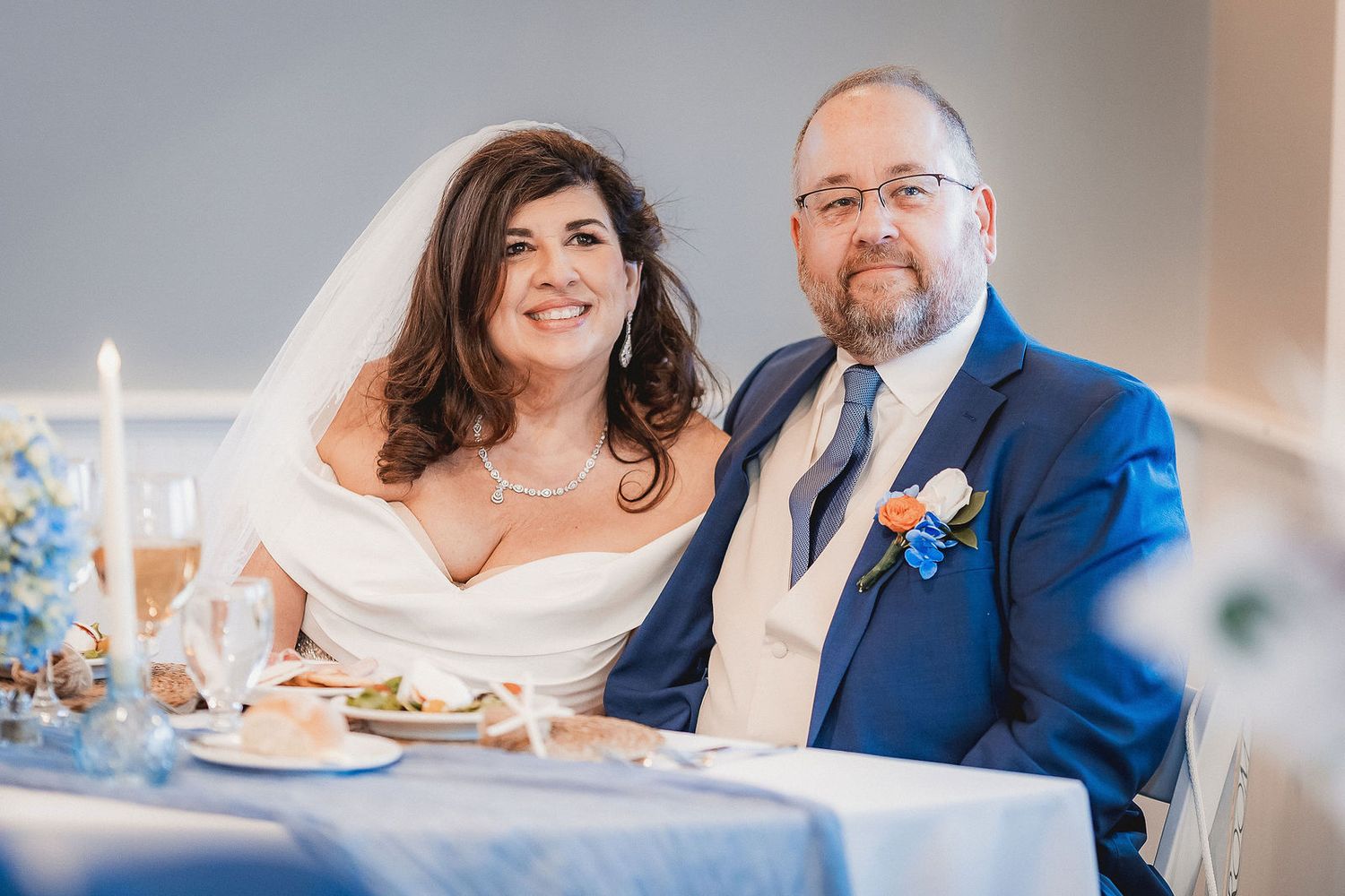 Bride and groom smiling together at wedding reception sweetheart table with candles.