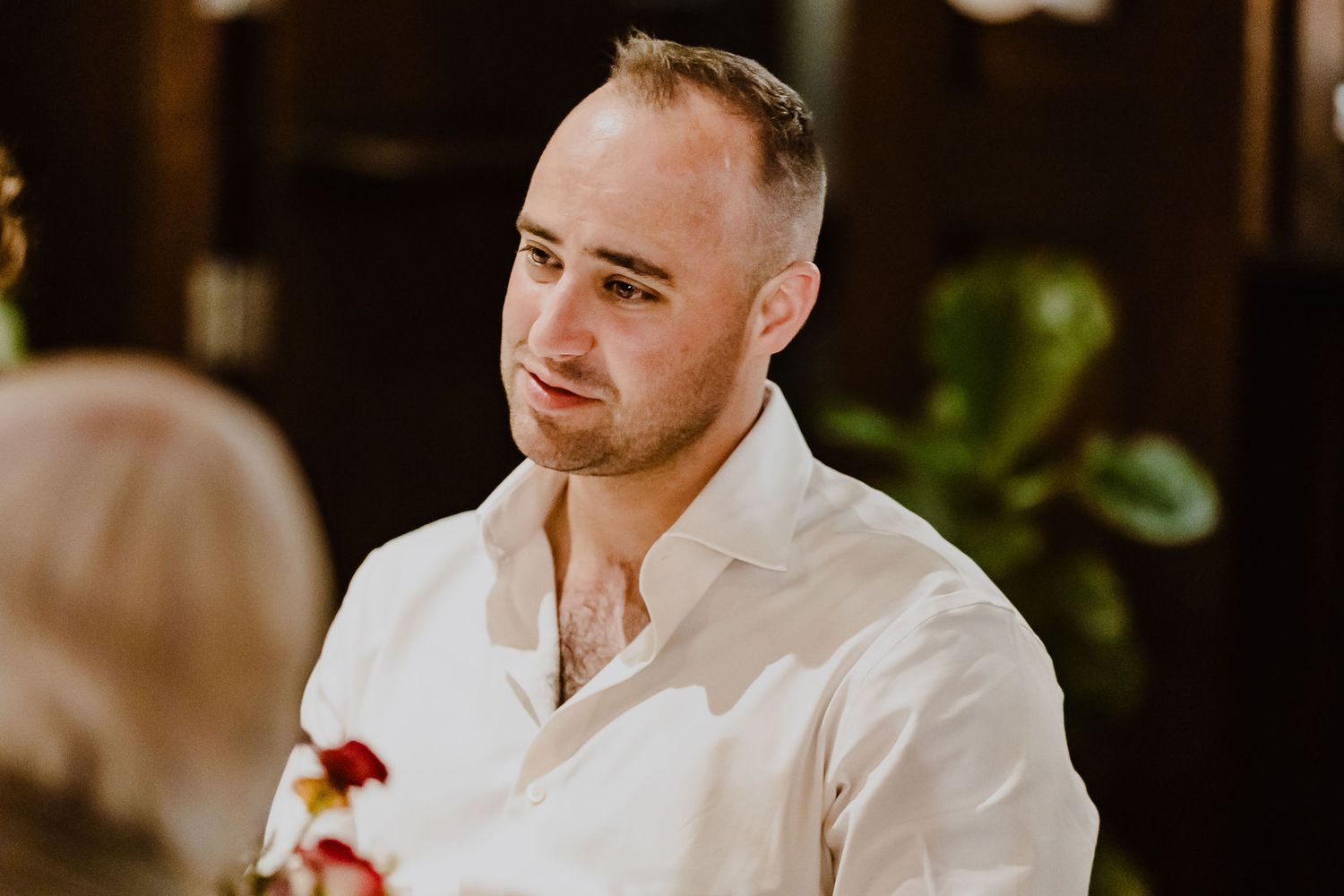 Emotional groom in white shirt listens attentively during wedding ceremony with soft lighting.