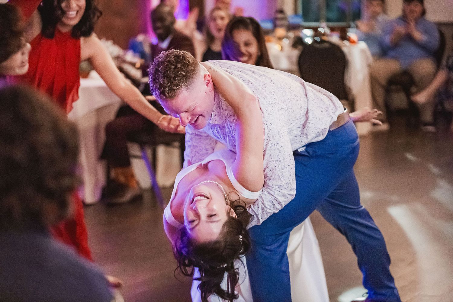 Groom dramatically dipping bride during energetic wedding reception dance performance.