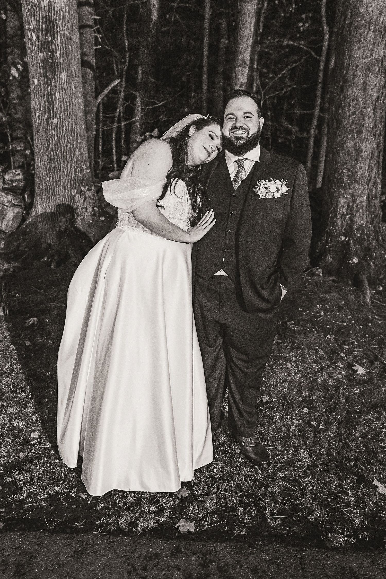 Black and white portrait of smiling bride and groom embracing in a wooded setting.