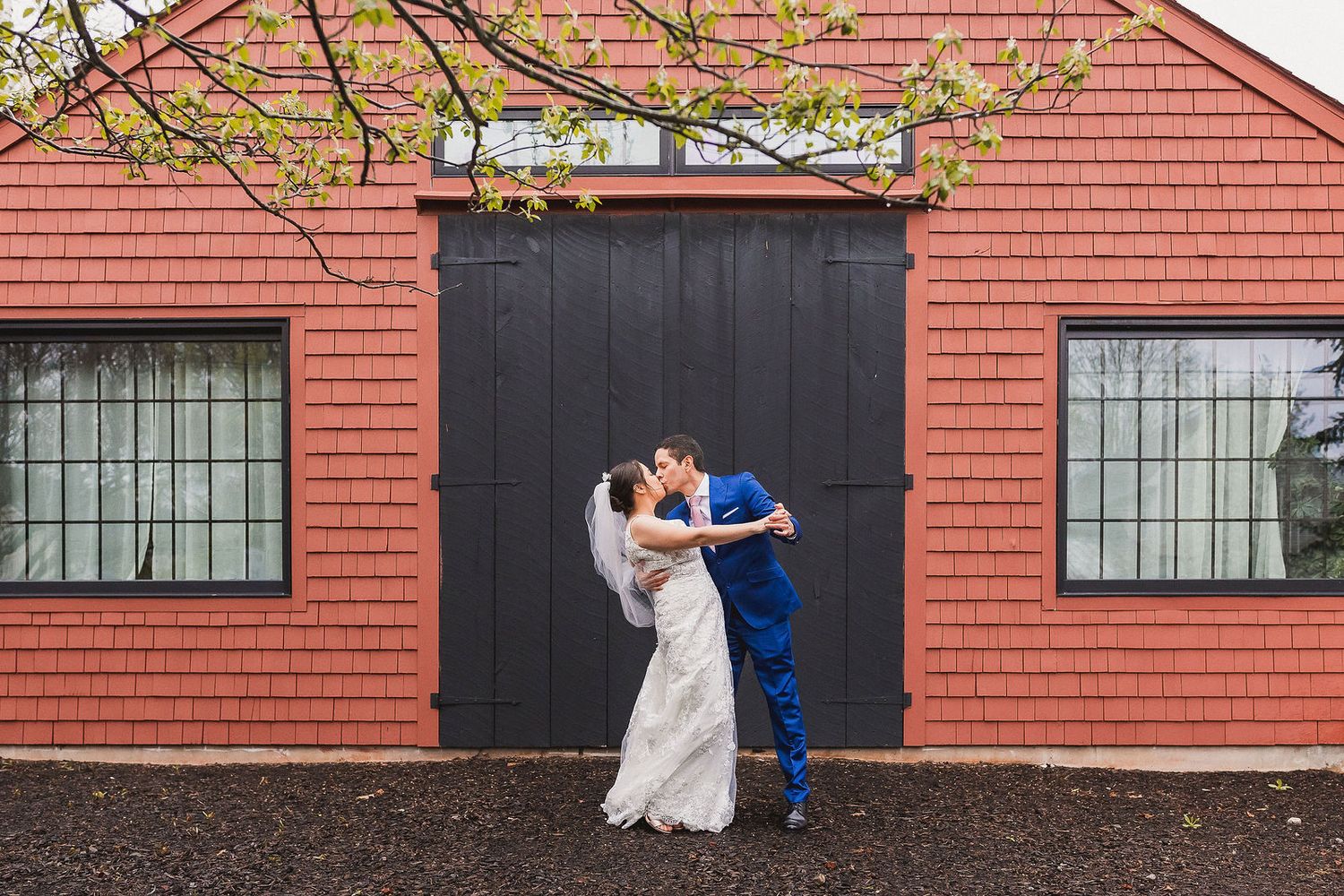 Newlyweds sharing passionate kiss in front of red building with black doors.