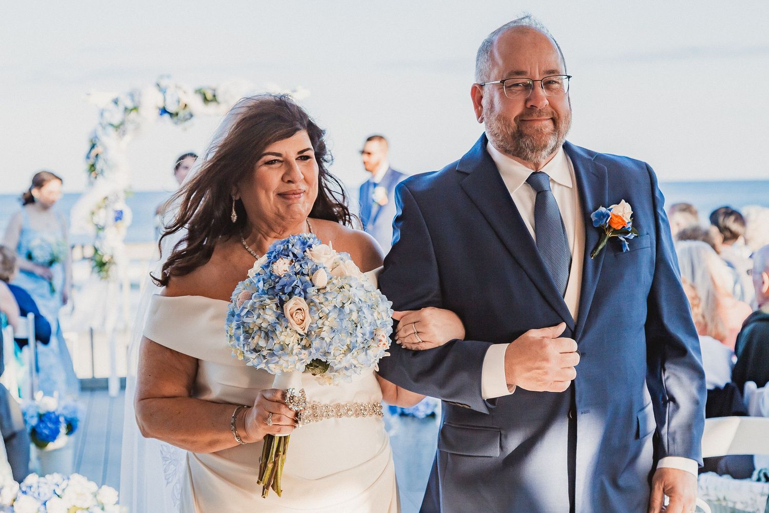 Bride and groom walking down the aisle at an outdoor beach wedding ceremony with blue floral decorations.