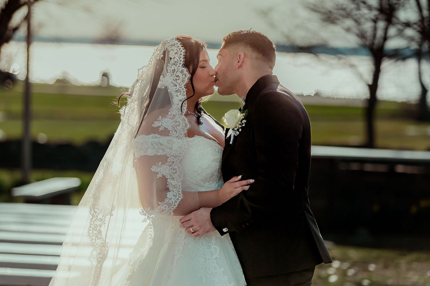 Bride and groom sharing a romantic kiss outdoors, bride wearing lace cathedral veil.