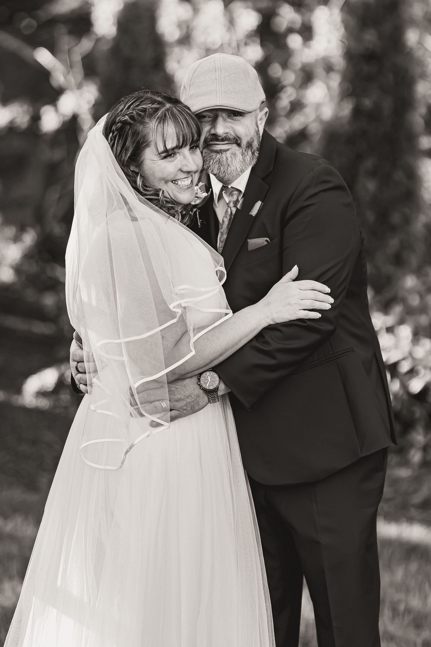 Black and white portrait of smiling bride and bearded groom embracing outdoors on wedding day.