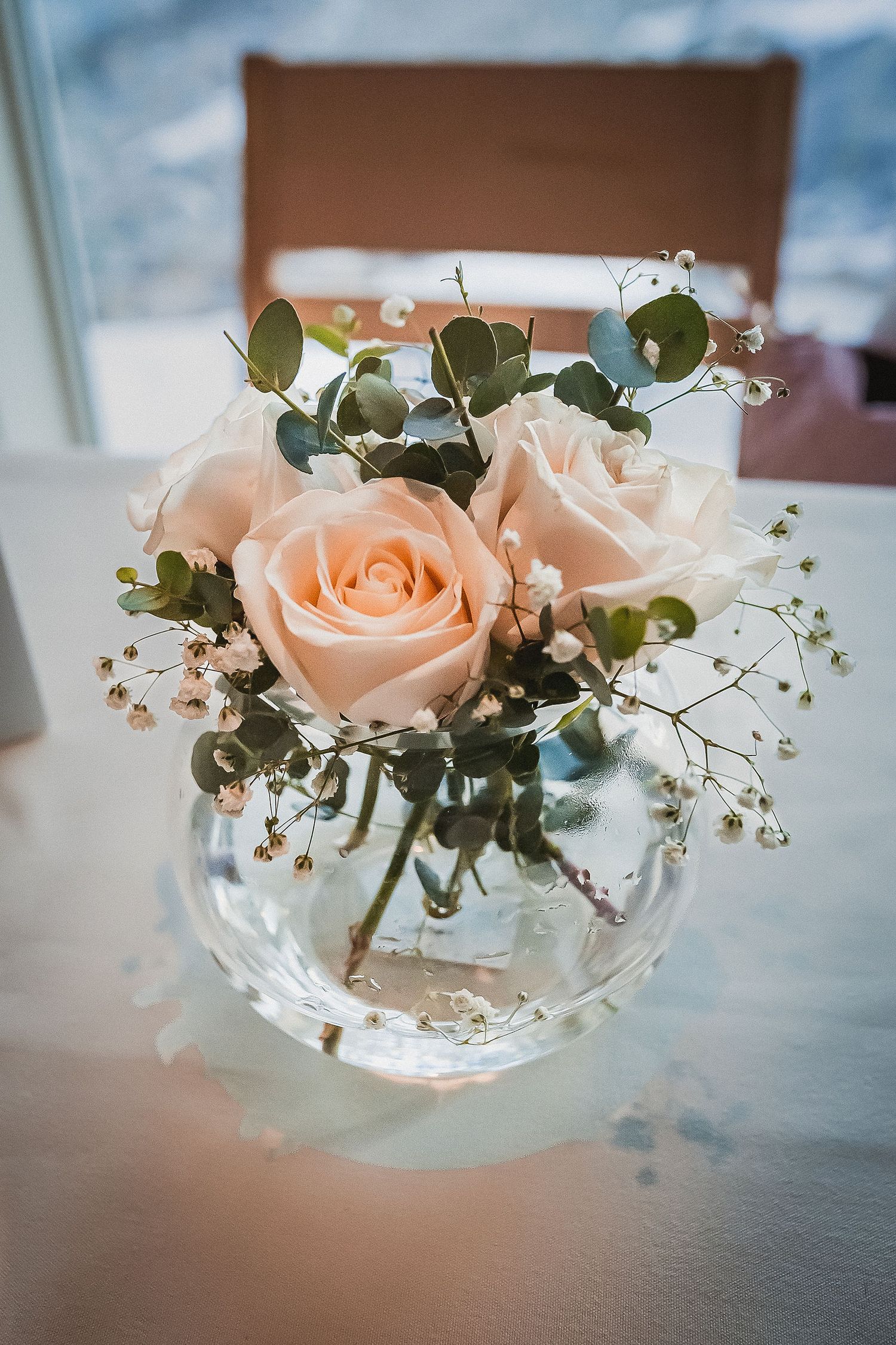 Elegant wedding centerpiece of peach roses and eucalyptus in a round glass vase.
