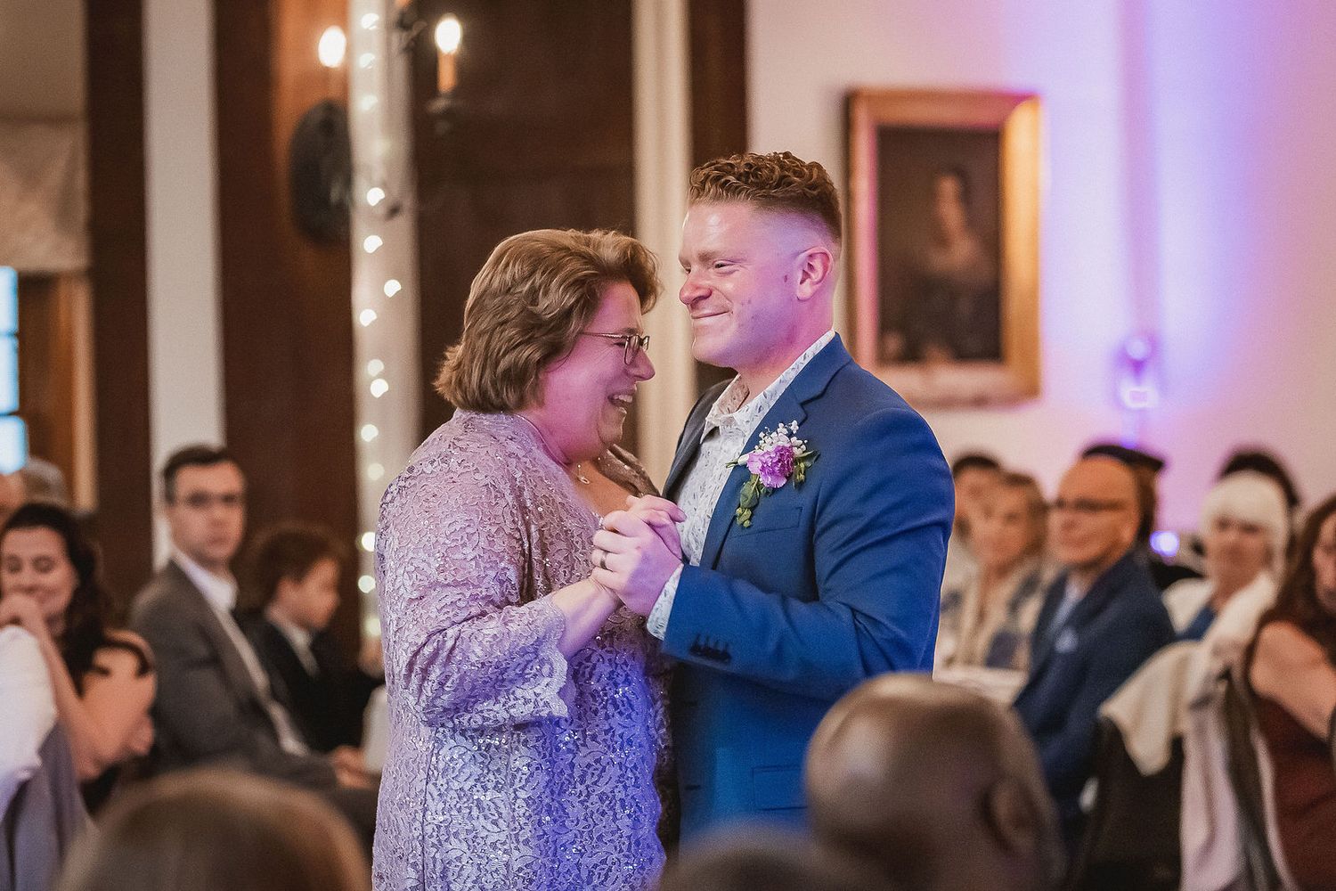 Groom in blue suit shares a dance with his mother at the wedding reception.