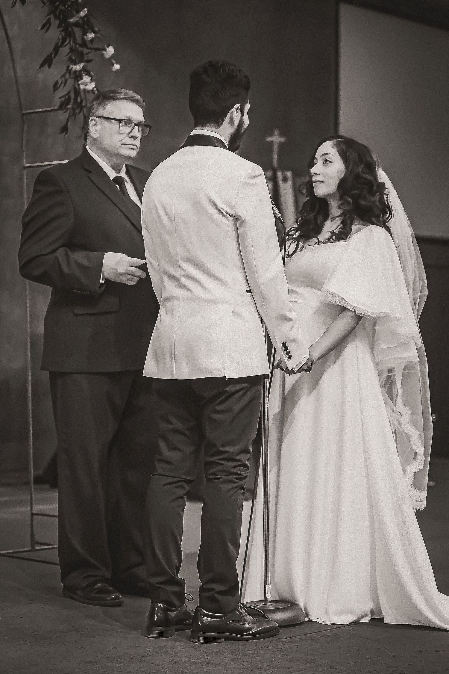 Black and white photo of bride and groom exchanging vows before officiant at altar.