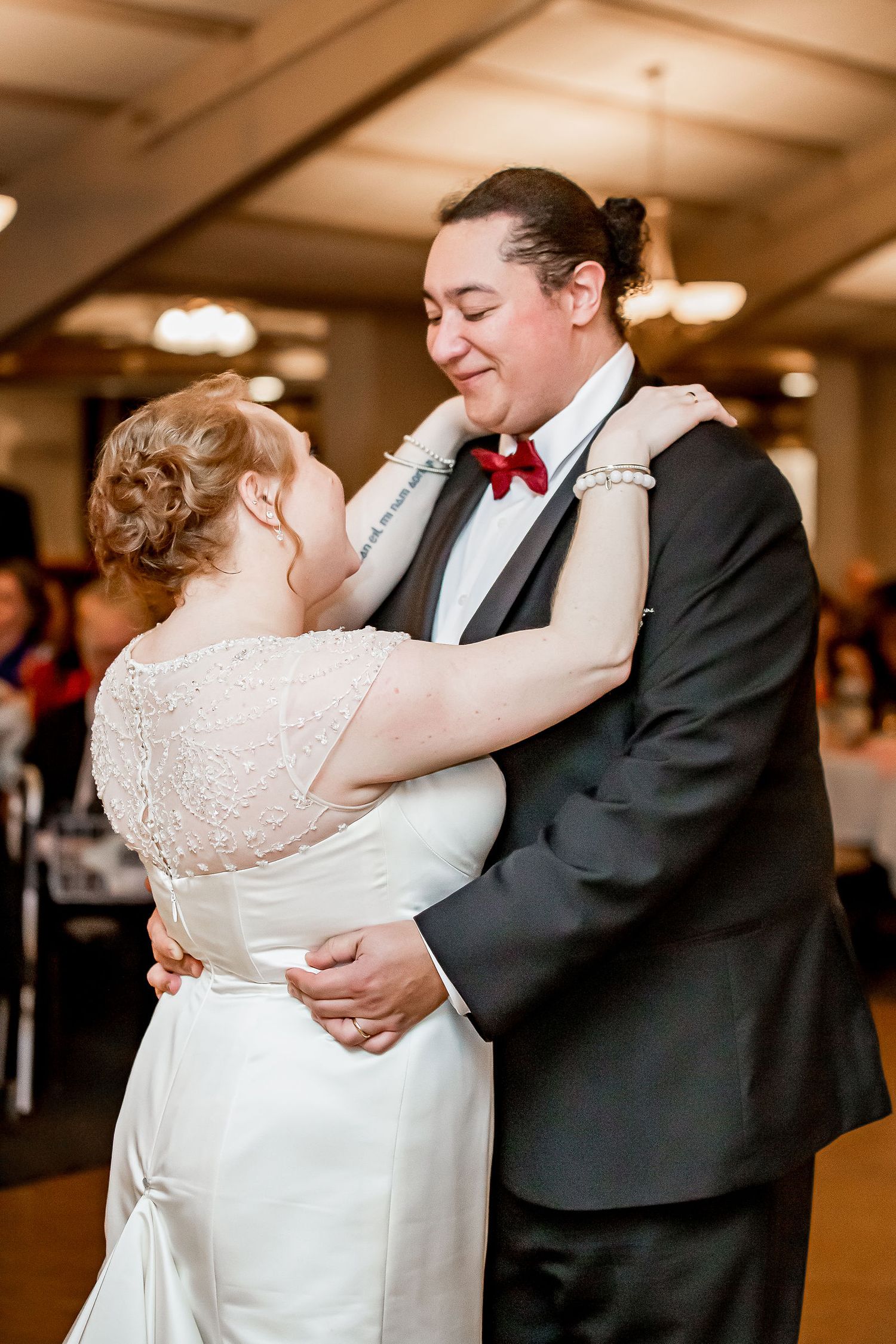 Bride and groom sharing their first dance, groom wearing black tuxedo with red bow tie.