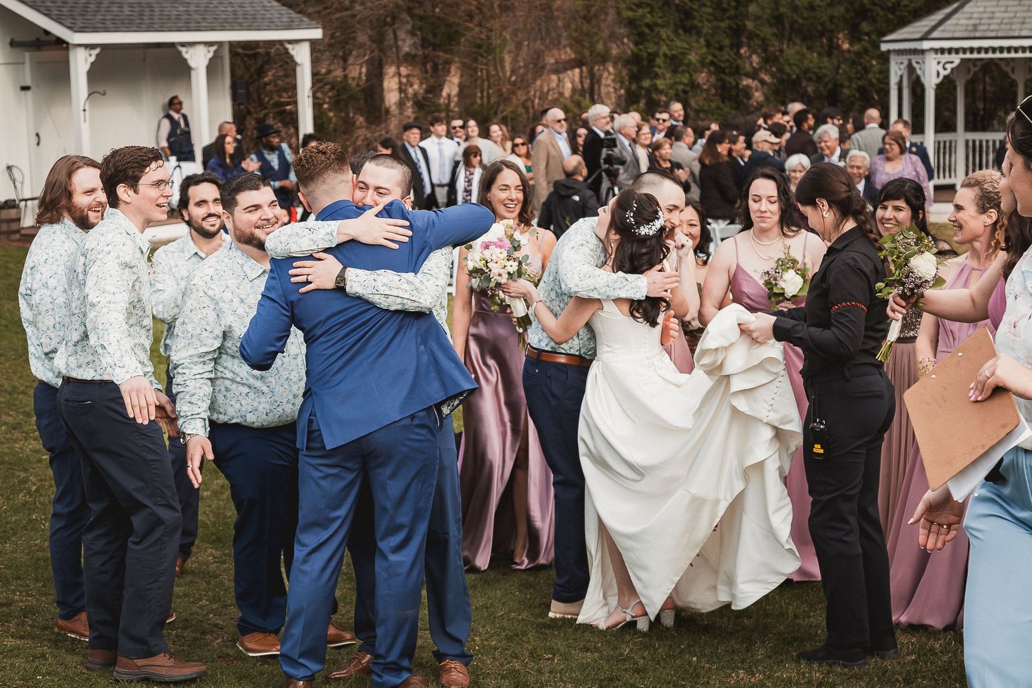 Newlyweds celebrating with wedding party after outdoor ceremony, bride in white gown surrounded by bridesmaids in pink dresses.