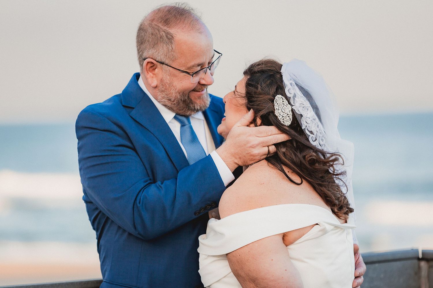 Groom tenderly touching brides face as they share an intimate moment at beachside wedding.