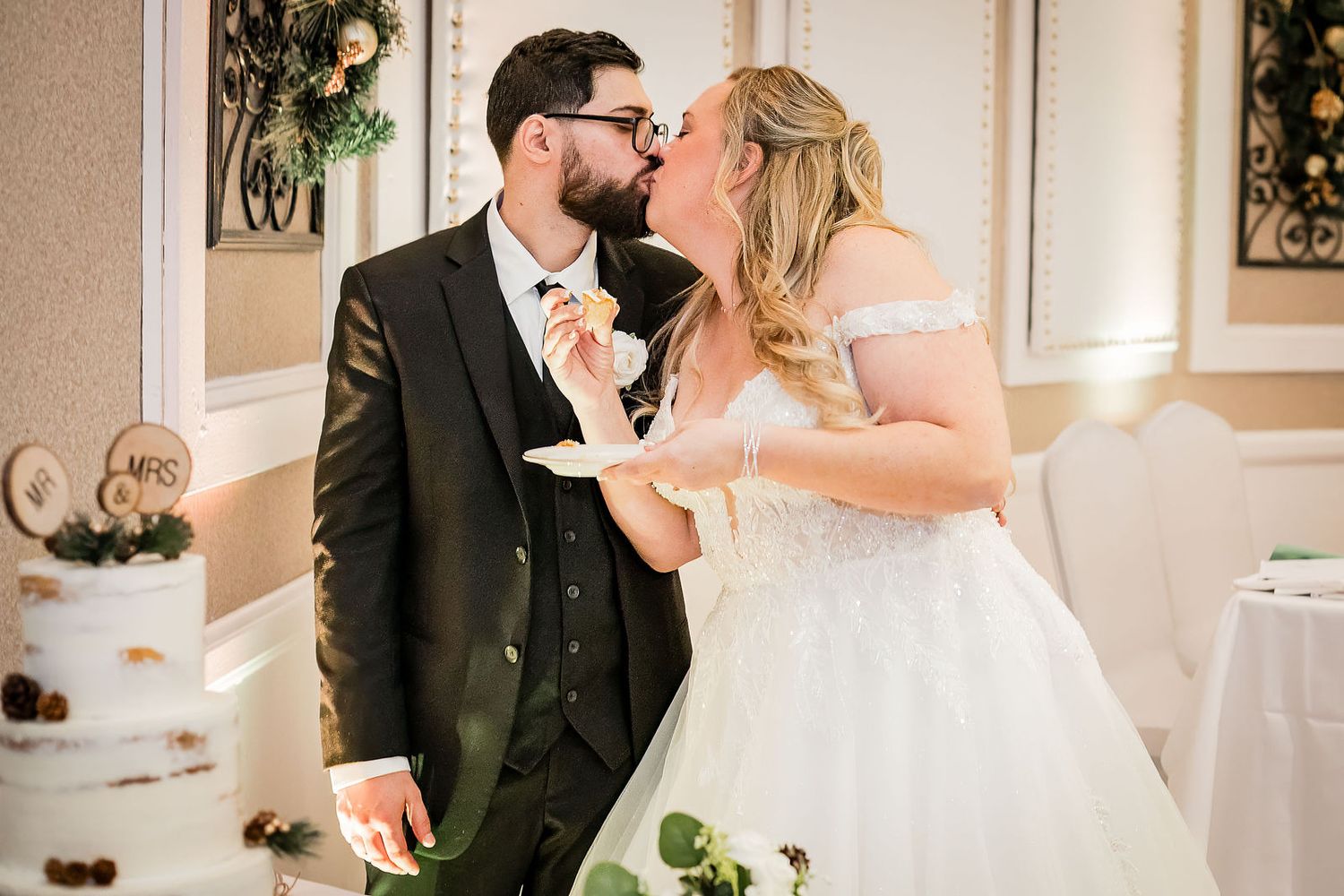 Bride and groom share a kiss while cutting their rustic naked wedding cake at reception.
