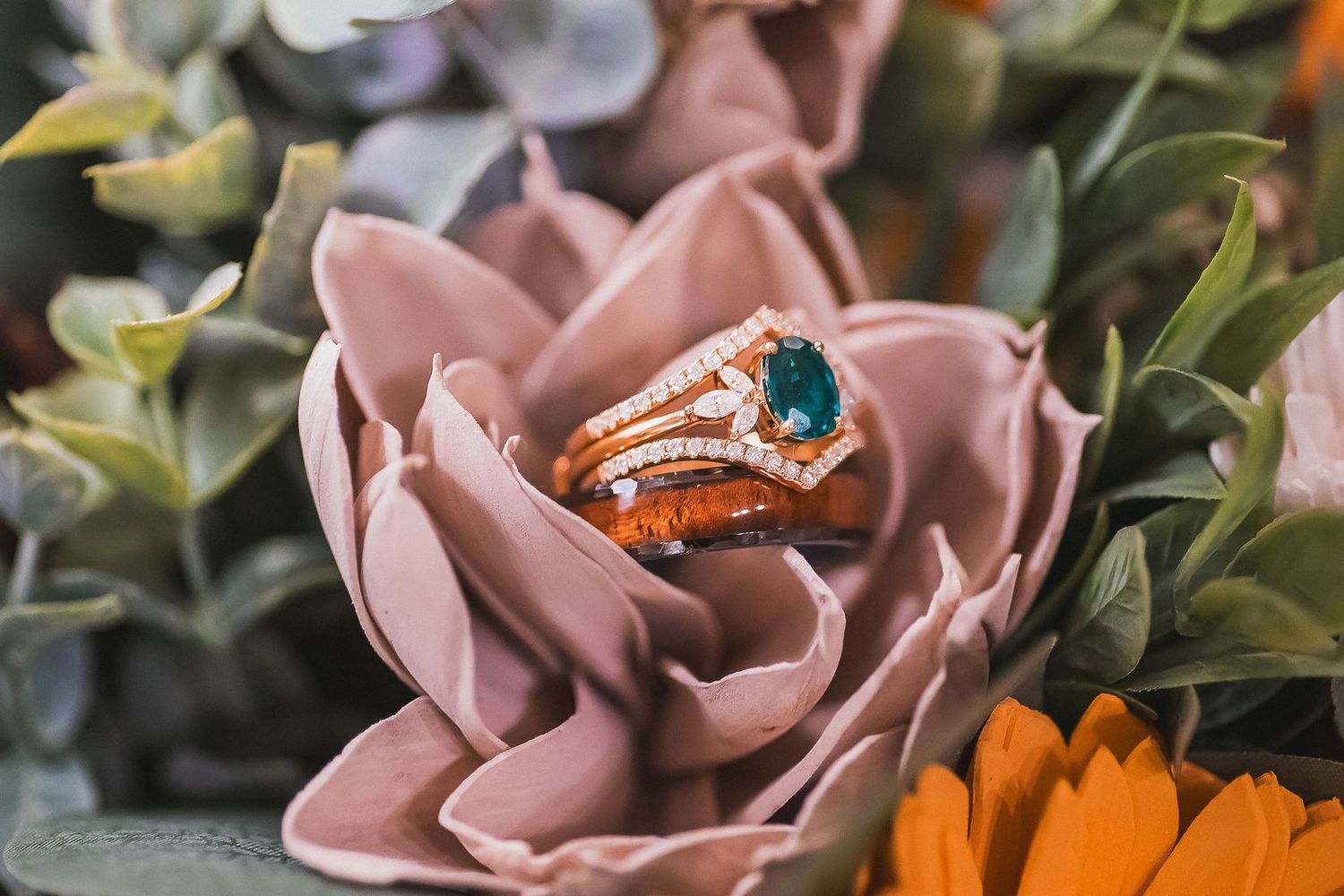 Rose gold wedding ring set with blue gemstone displayed on pink artificial flower.