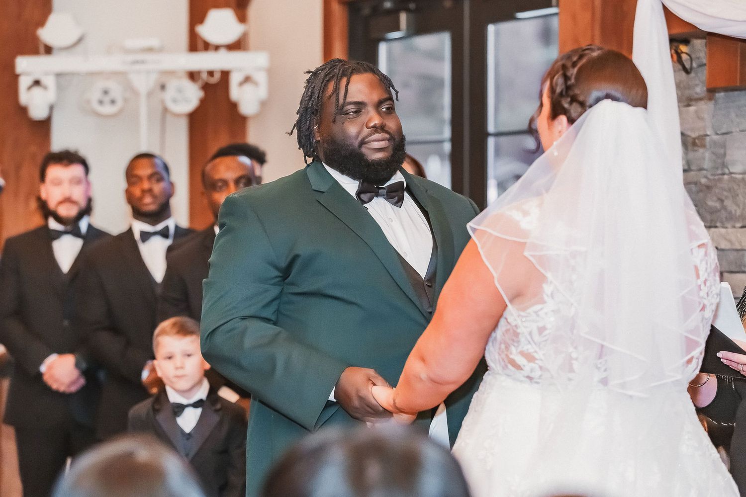 Groom in green tuxedo holds brides hands at altar during wedding ceremony in elegant venue.