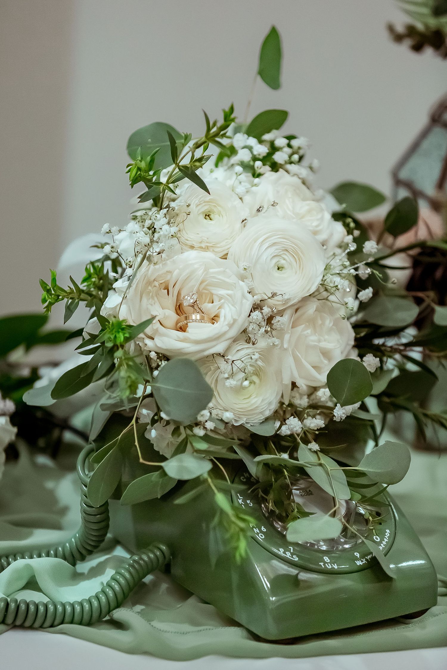 Elegant white rose and eucalyptus bridal bouquet arranged on vintage green rotary phone.
