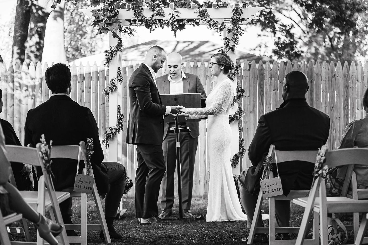 Black and white outdoor wedding ceremony with couple exchanging vows before officiant.