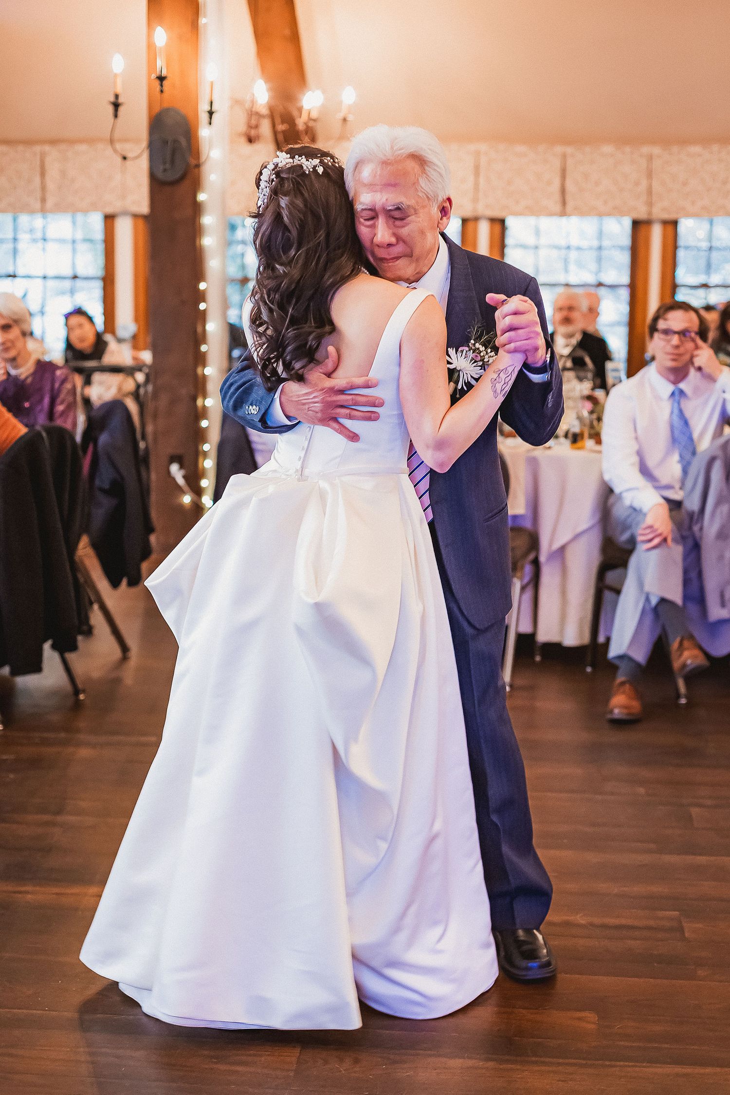 Bride and elderly man sharing an emotional father-daughter dance at wedding reception.