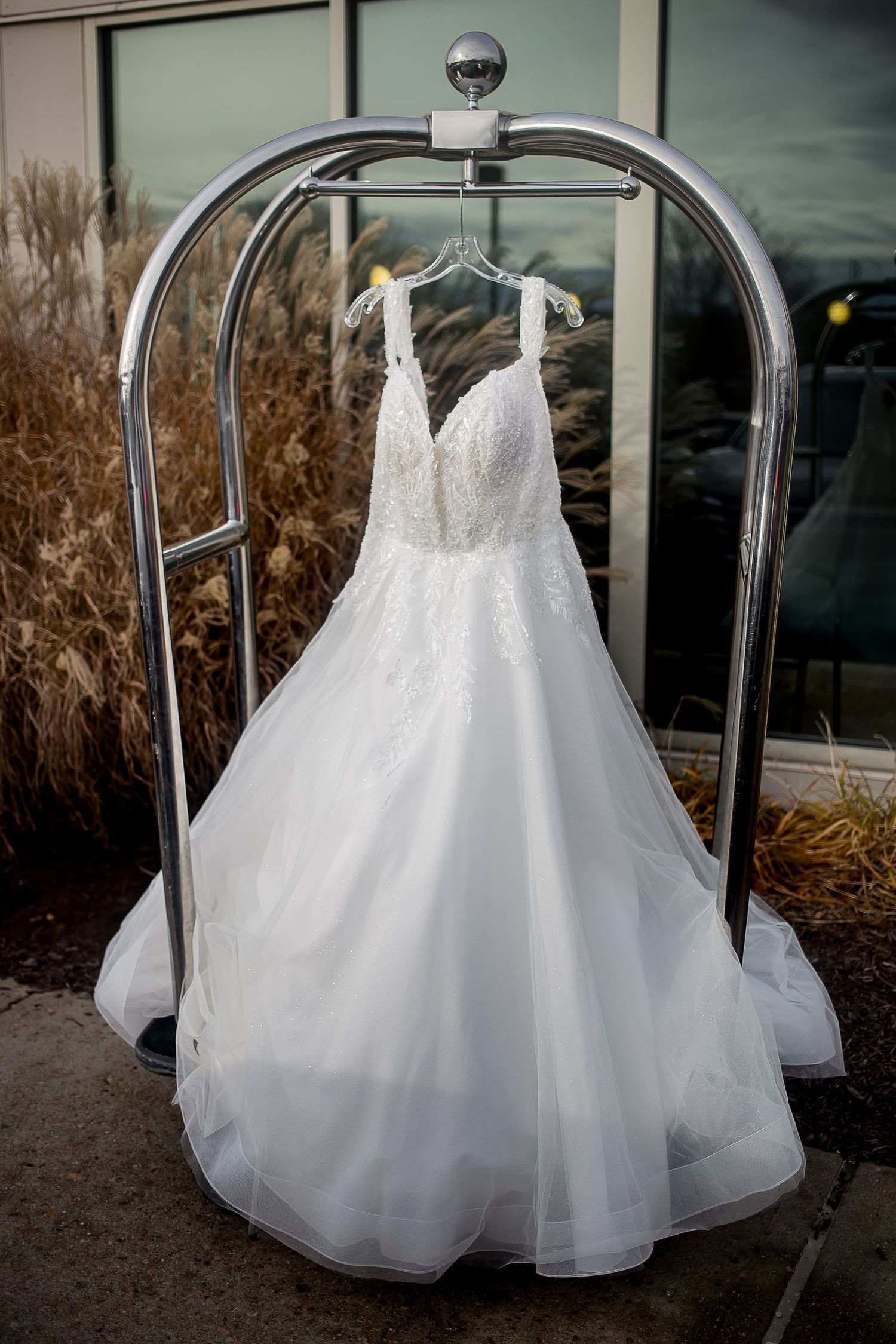 Beautiful white lace A-line wedding dress hanging on a luggage cart outside a venue.