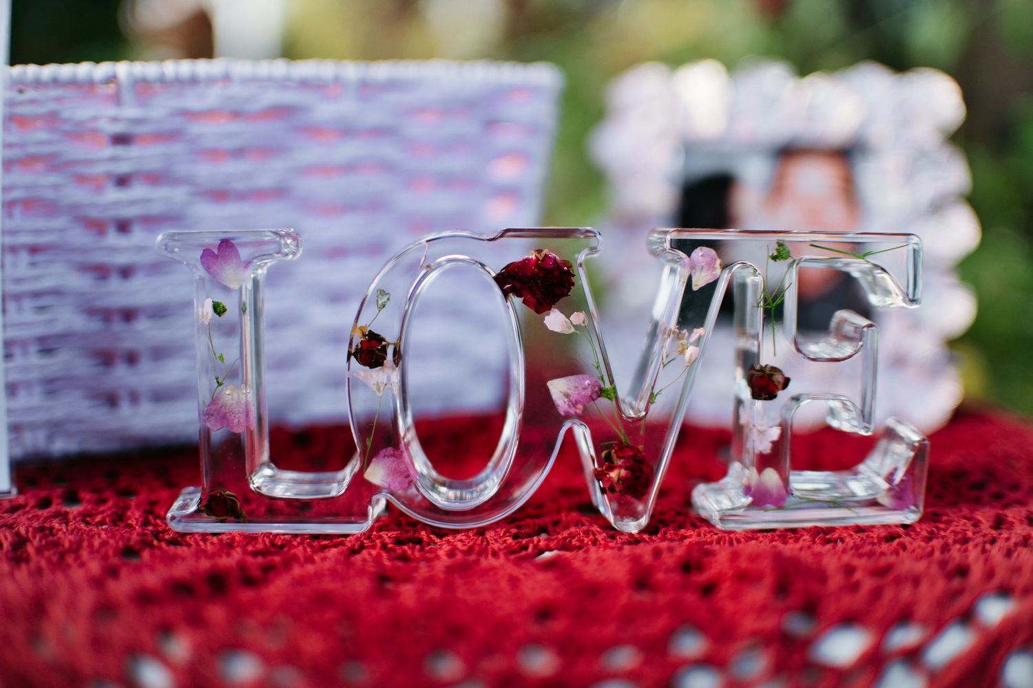 Clear glass LOVE letters filled with red roses displayed on a red crochet tablecloth at a wedding reception.