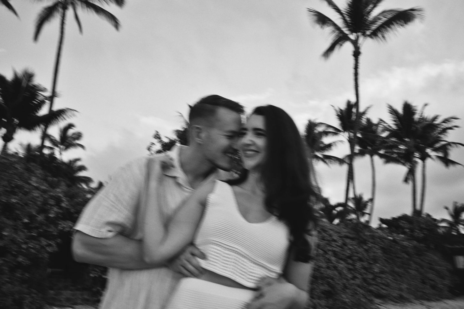 Black and white photo of couple laughing together near tropical palm trees.