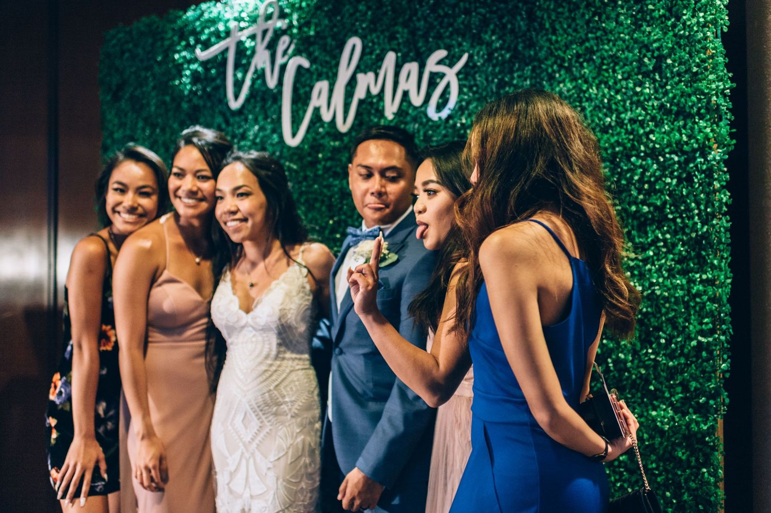 Wedding party members pose together in front of a green hedge wall with elegant signage.