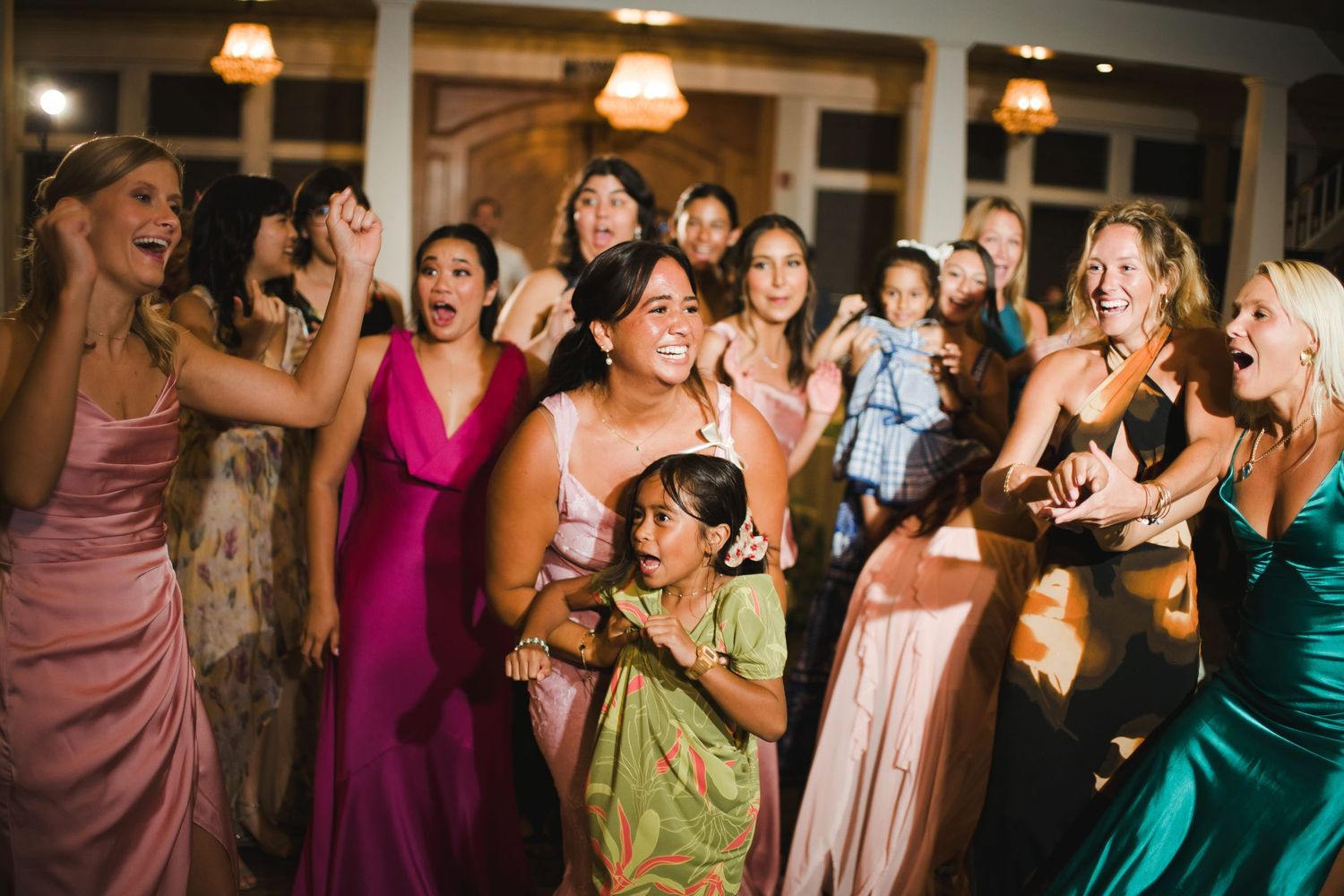 Bridesmaids in colorful gowns celebrate joyfully on the dance floor at a lively wedding reception.