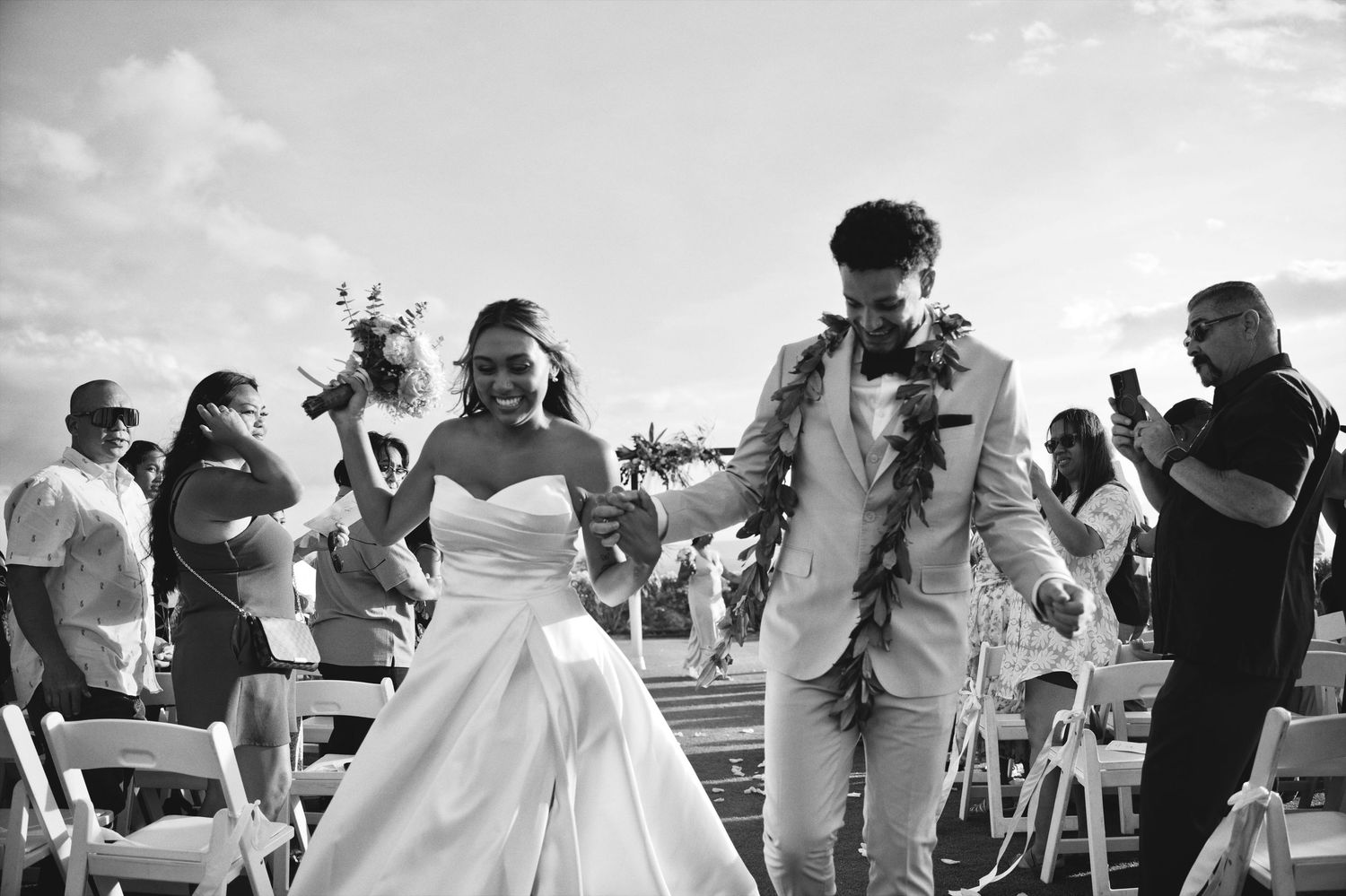 Black and white photo of a newlywed couple walking down the aisle at an outdoor wedding ceremony.