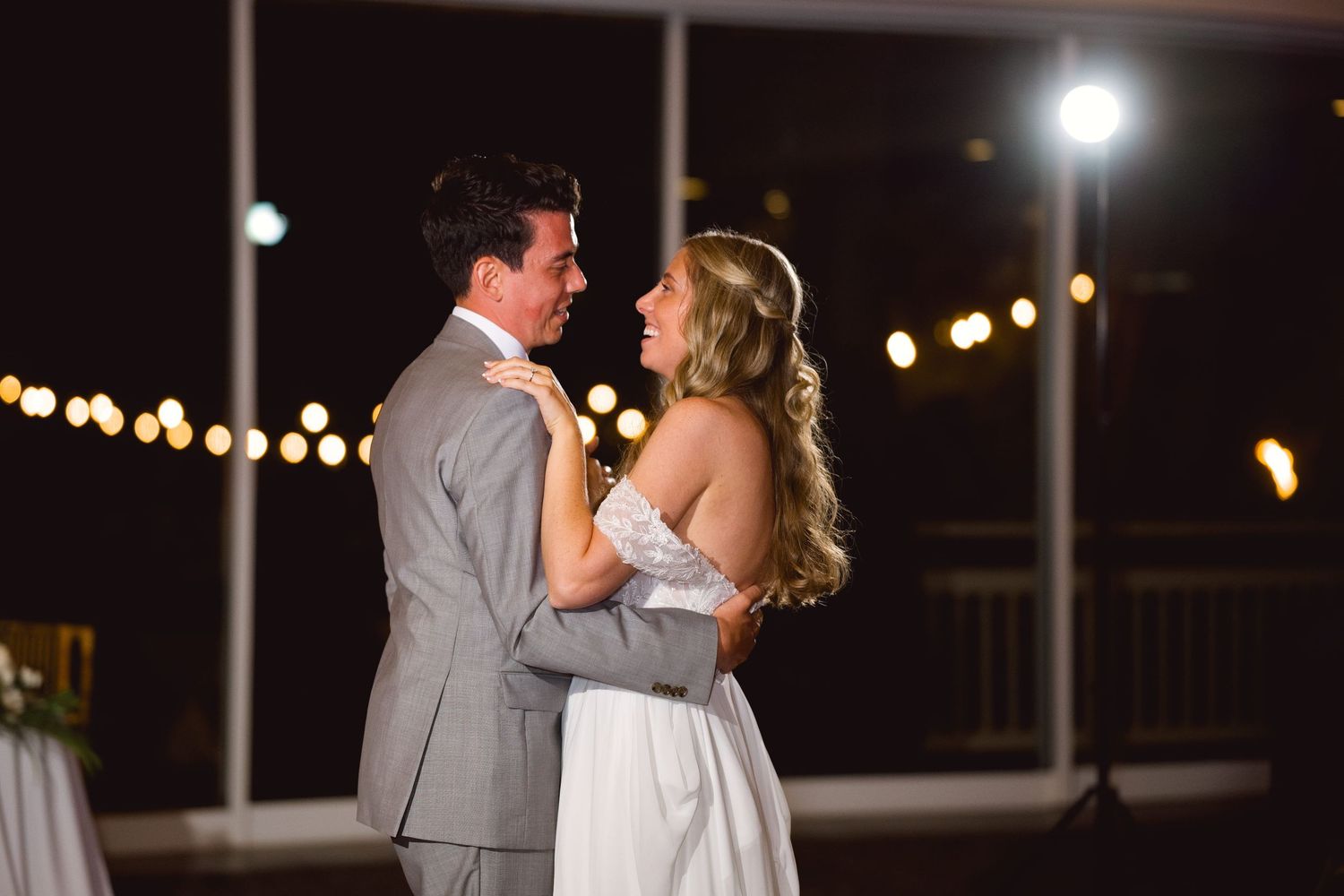 Bride and groom share their first dance under romantic string lights at an outdoor wedding reception at night.