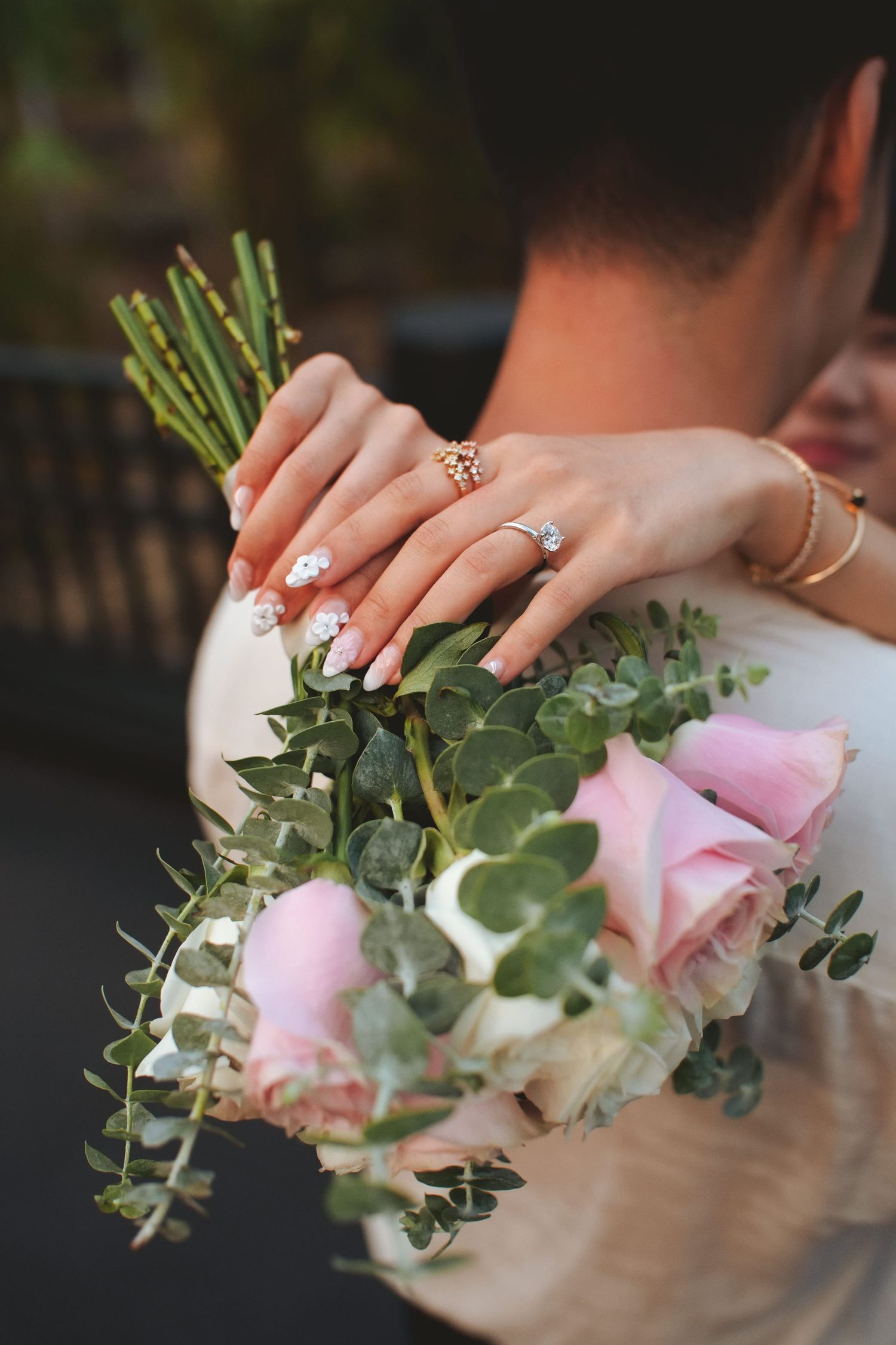 Bride holding pink roses bouquet while embracing groom, showcasing diamond engagement ring and elegant nail art.