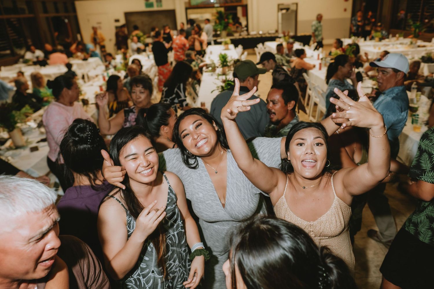 Wedding reception guests dancing and celebrating on a crowded dance floor at an indoor venue.