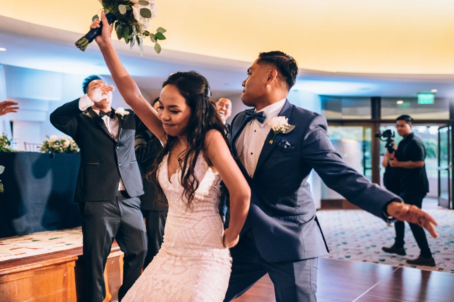 Wedding party performs synchronized dance routine in modern reception space with dramatic lighting.