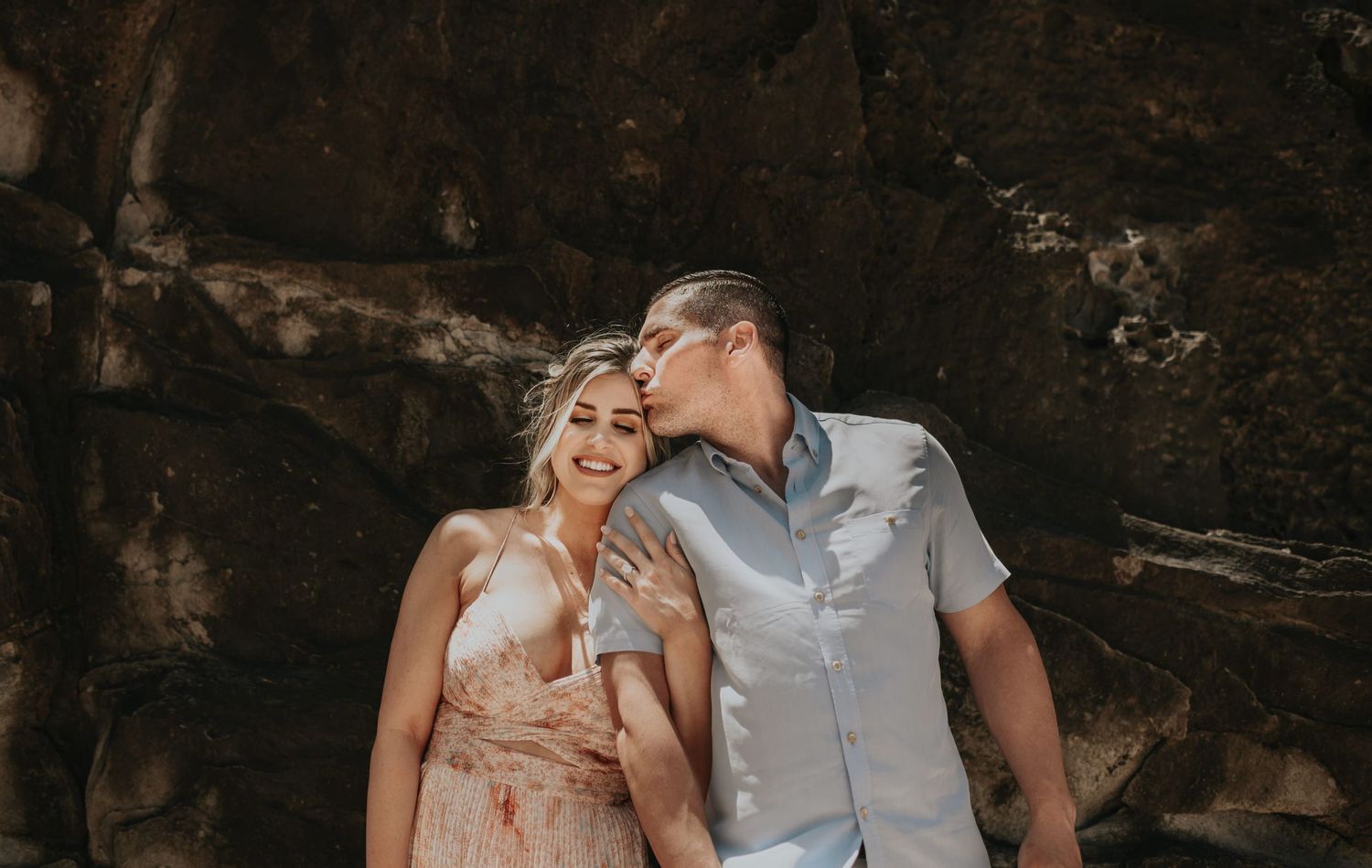 Man kissing woman on cheek as they pose together in front of rocky backdrop.