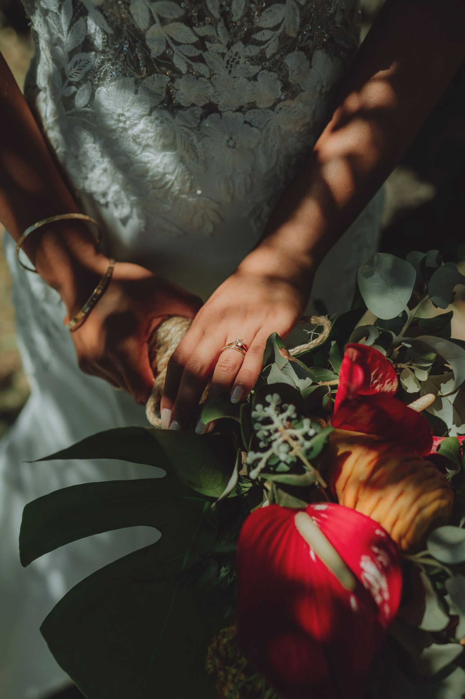 Close-up of bride's hands holding a vibrant red tropical wedding bouquet with engagement ring visible.